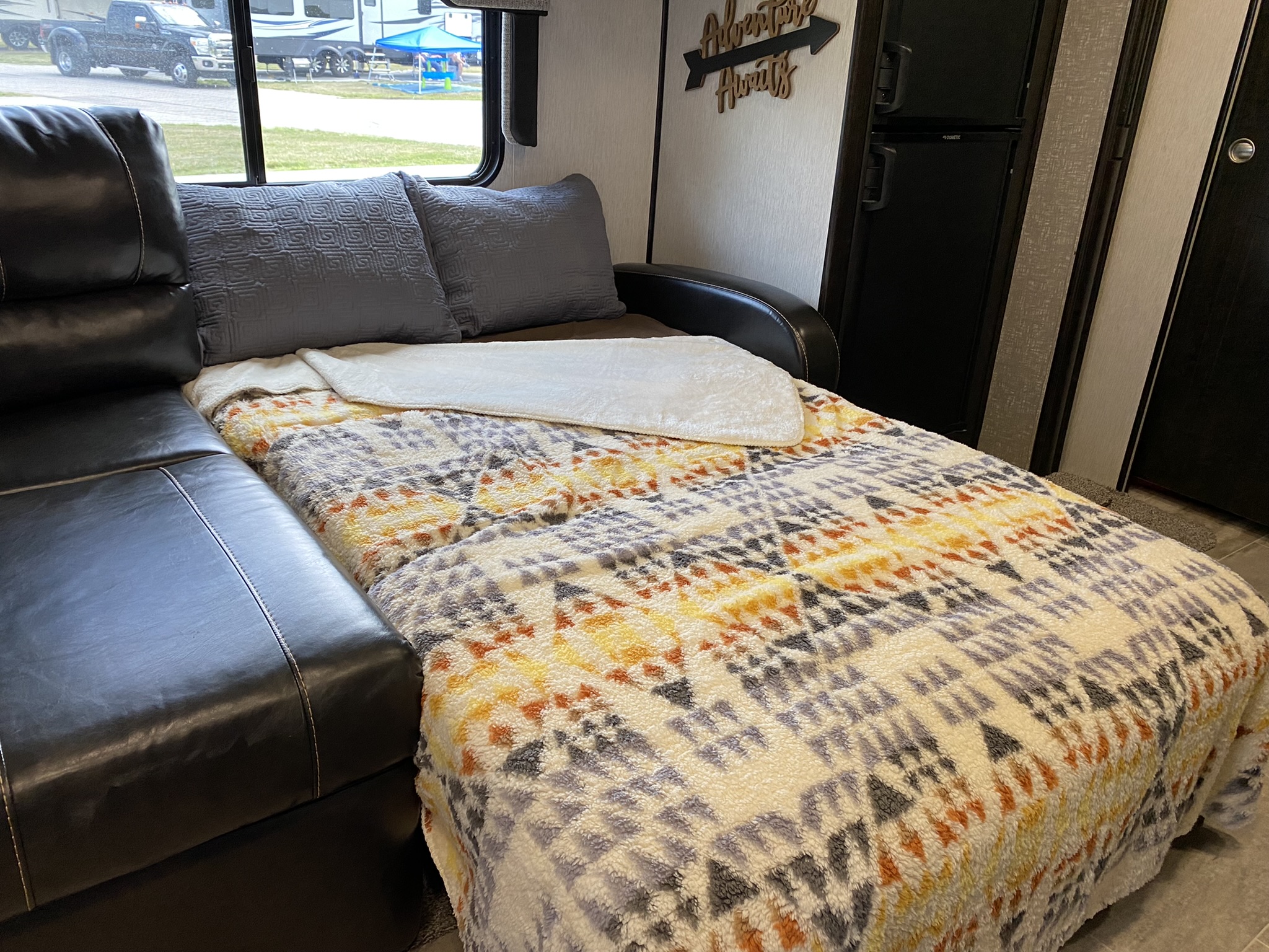 Comfortable pull-out bed in an RV rental, covered with cozy blankets and pillows. Perfect for travel adventures!. Heartland RVs North Trail 2019