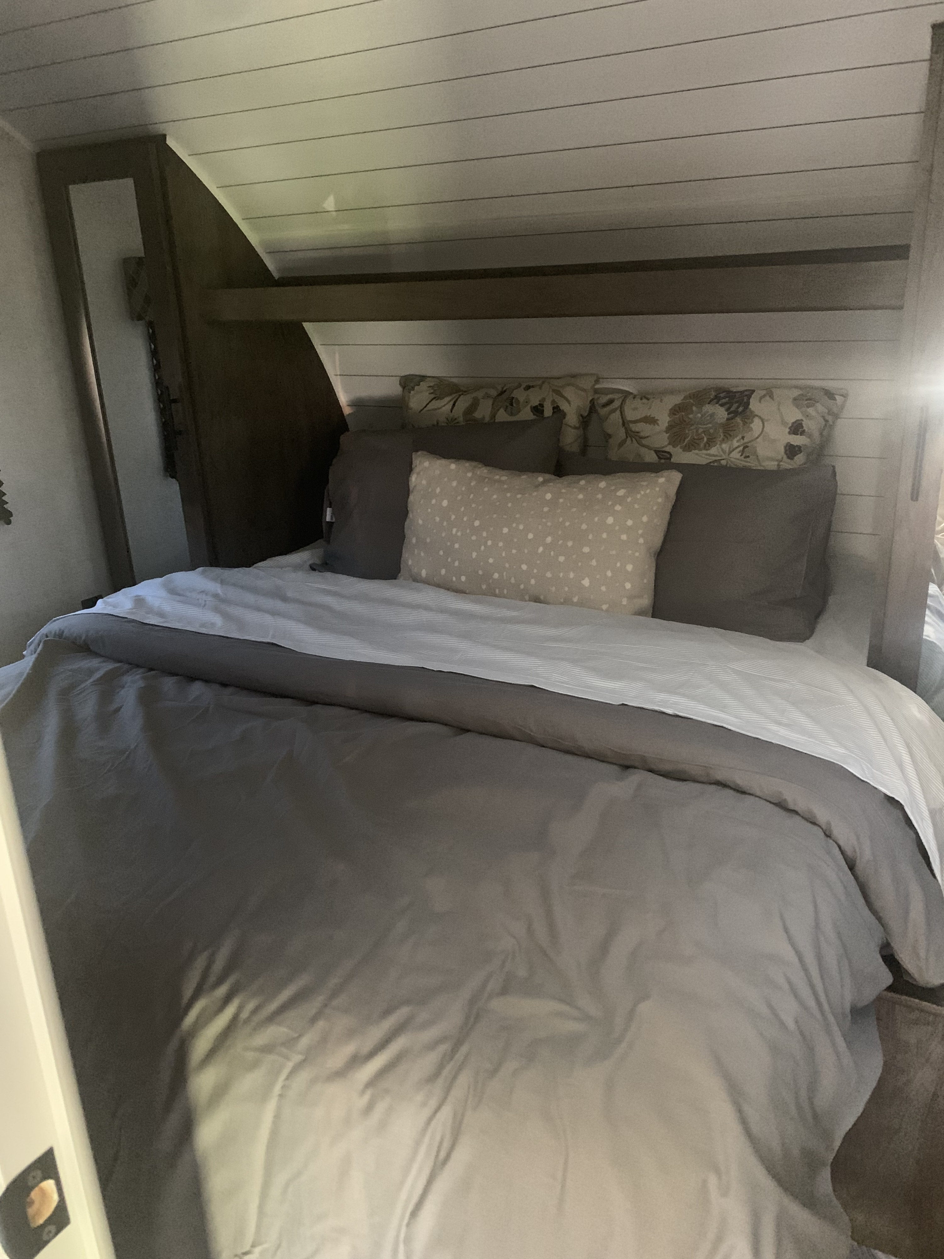 Cozy RV rental bedroom featuring a neatly made bed with grey bedding and decorative pillows in a compact sleeping area.. Forest River EVO T2400BH 2021