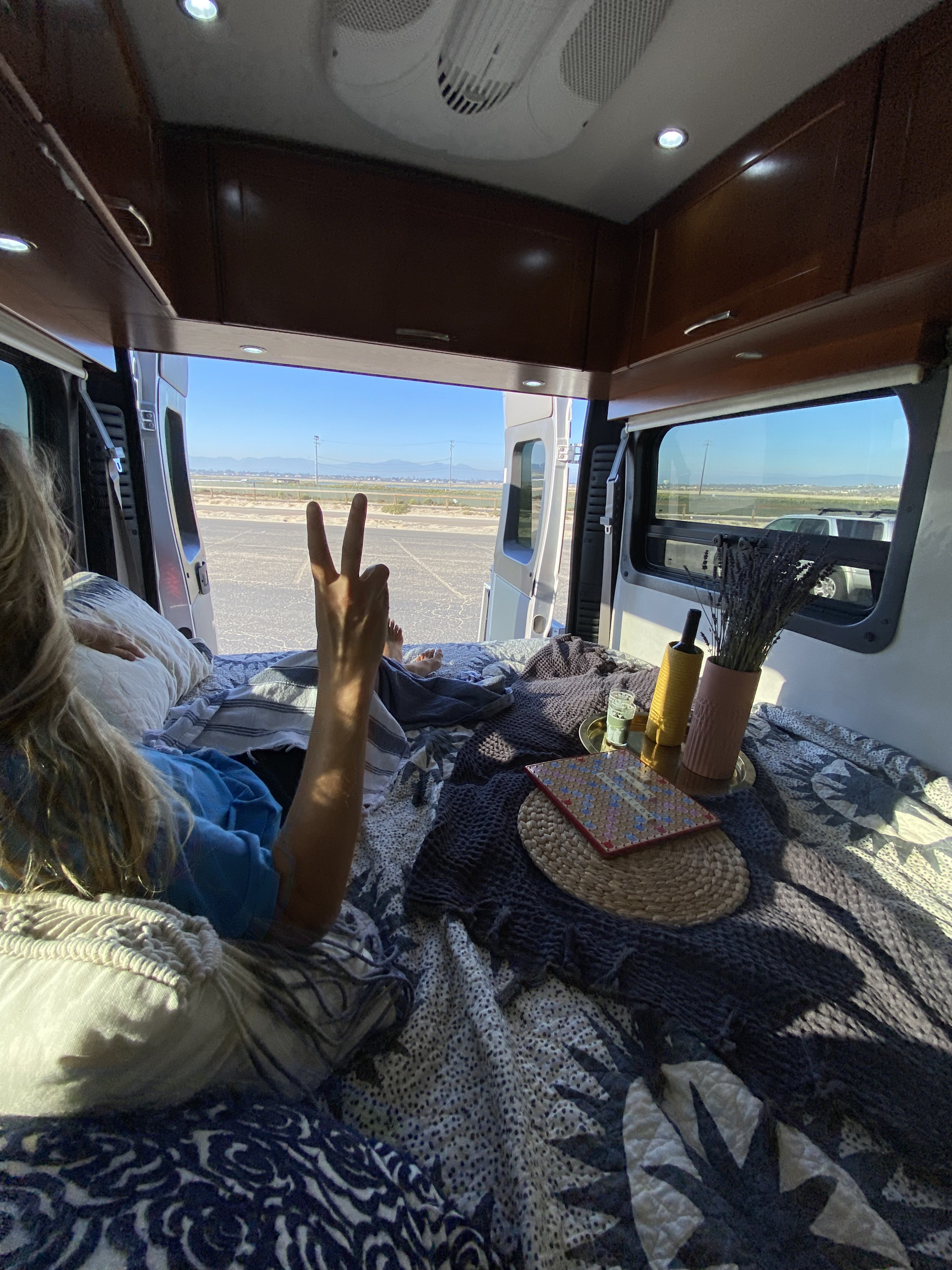 Relaxing inside an RV rental with open doors, showing a peace sign, comfy bed, and a scenic outdoor view.. Pleasure-Way Pleasure-Way Class B 2016
