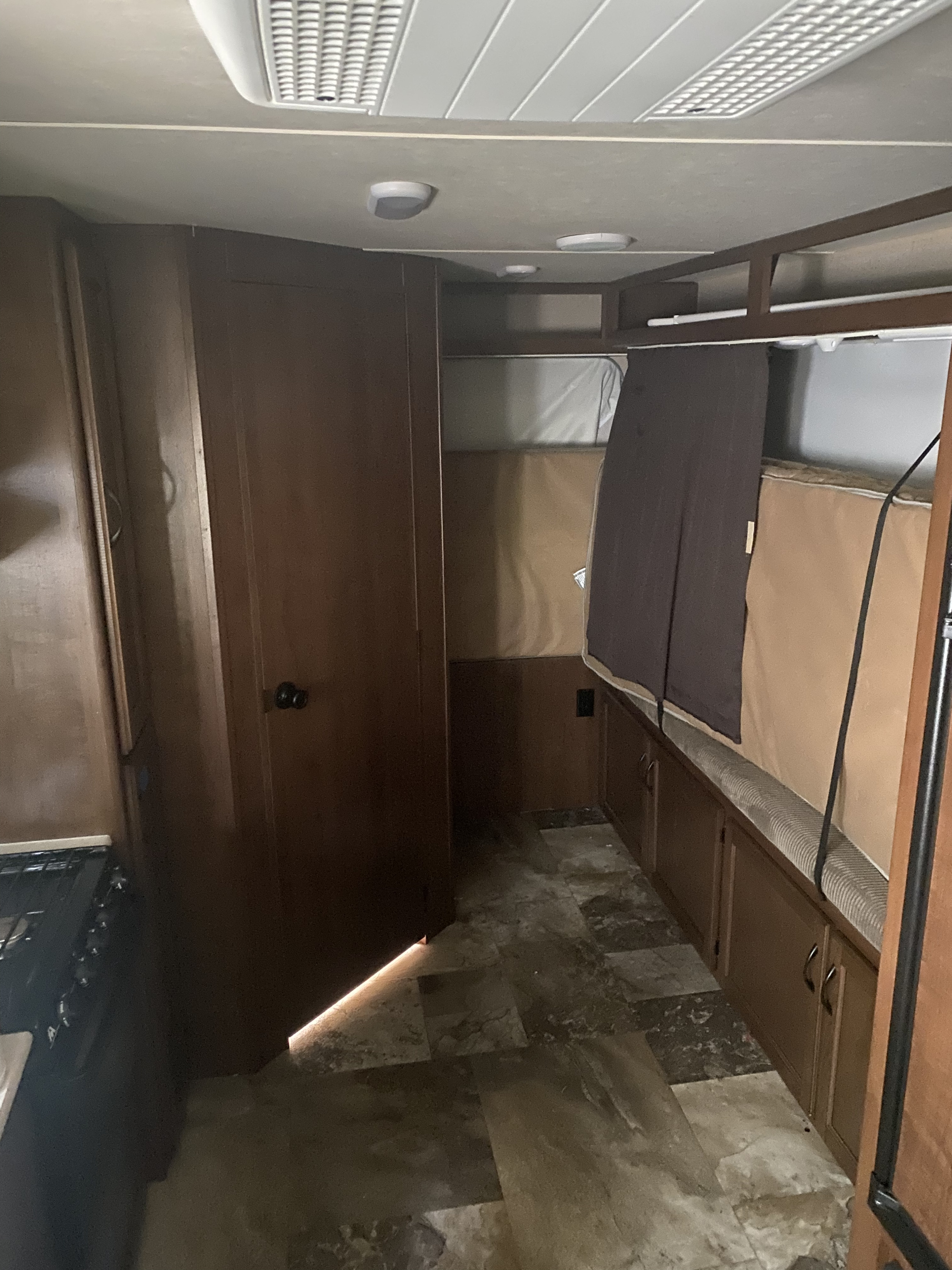 Interior of an RV rental: wood-toned walls, bunk beds with privacy curtains, tile floor, and ceiling lights, hint of kitchen.. Jayco Jay Feather Ultra Lite 2015