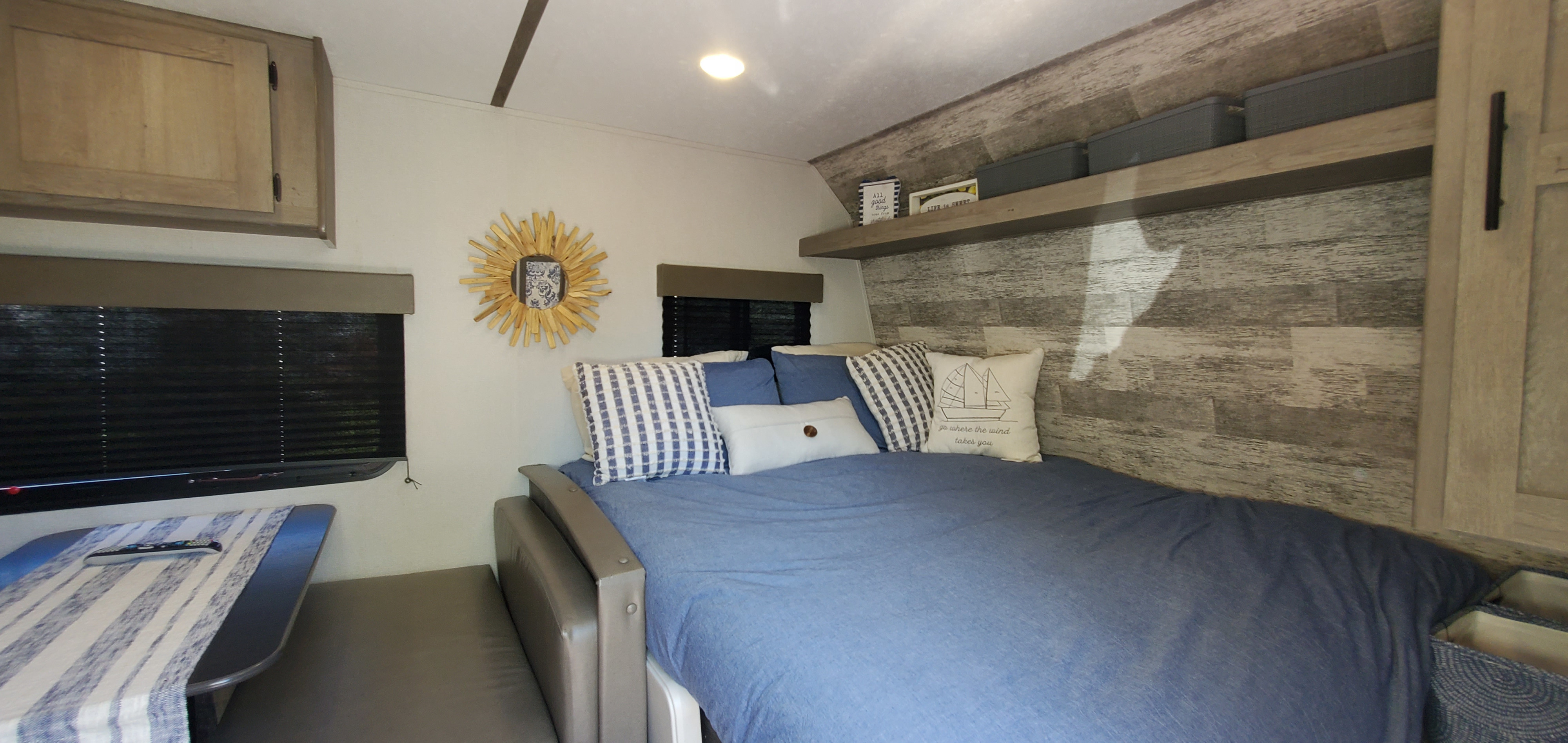 Inside an RV rental, showing a cozy bedroom with blue bedding, nautical pillows, wood-look walls, and functional storage.. Keystone RV Springdale 2021
