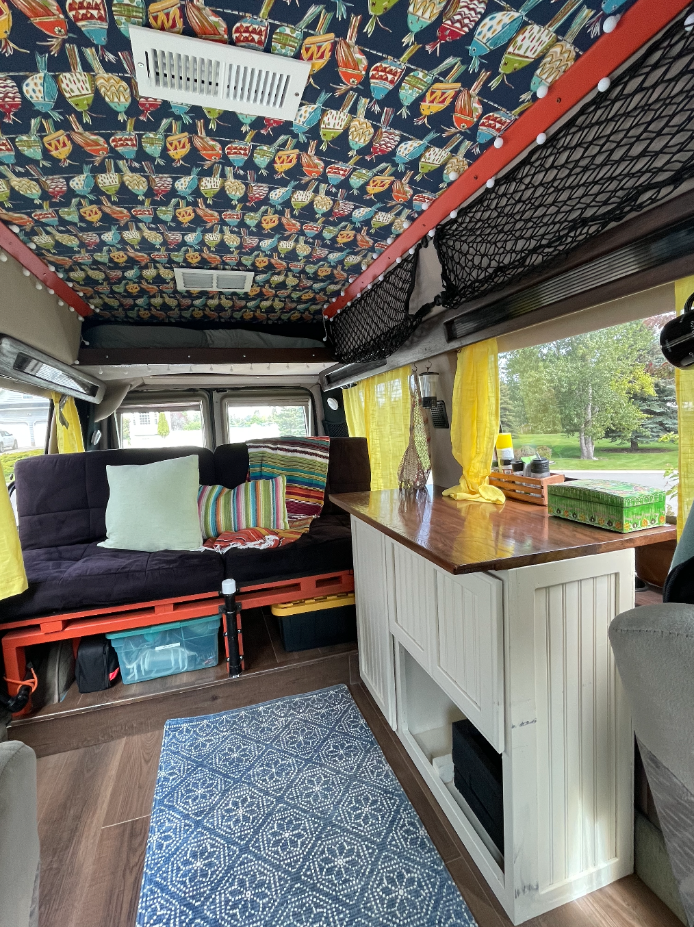 RV rental: Inside a cozy camper van featuring a vibrant bird-patterned ceiling, comfy futon, wood counter, and storage.. Ford Econoline 2006
