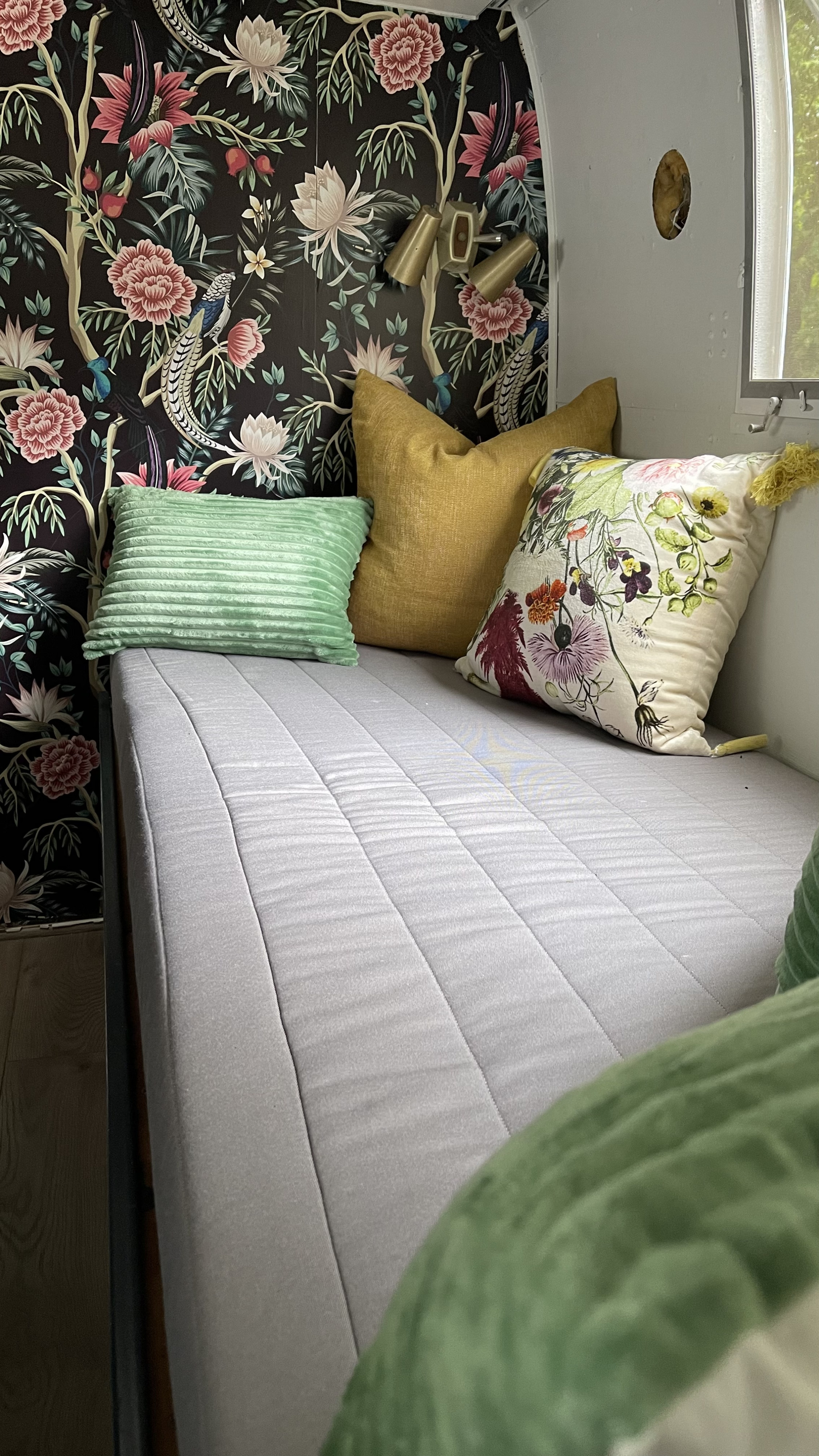 Discover this vibrant RV rental's cozy sleeping area, featuring floral wallpaper & comfy pillows.. Airstream Ambassador 1968