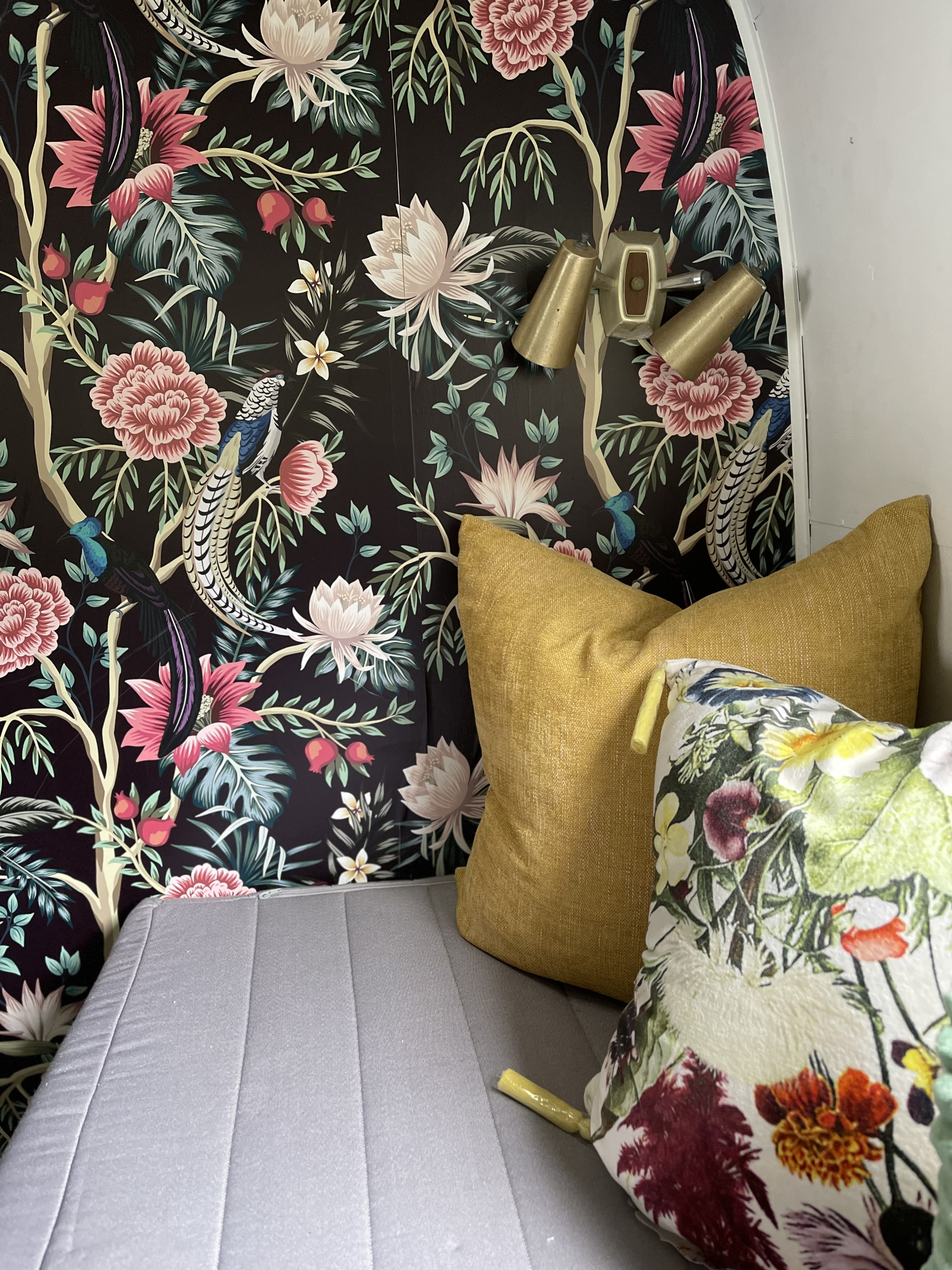 Inside this **RV rental**, vibrant floral and bird wallpaper, brass lights, and cozy grey seating with colorful pillows create a striking interior.. Airstream Ambassador 1968