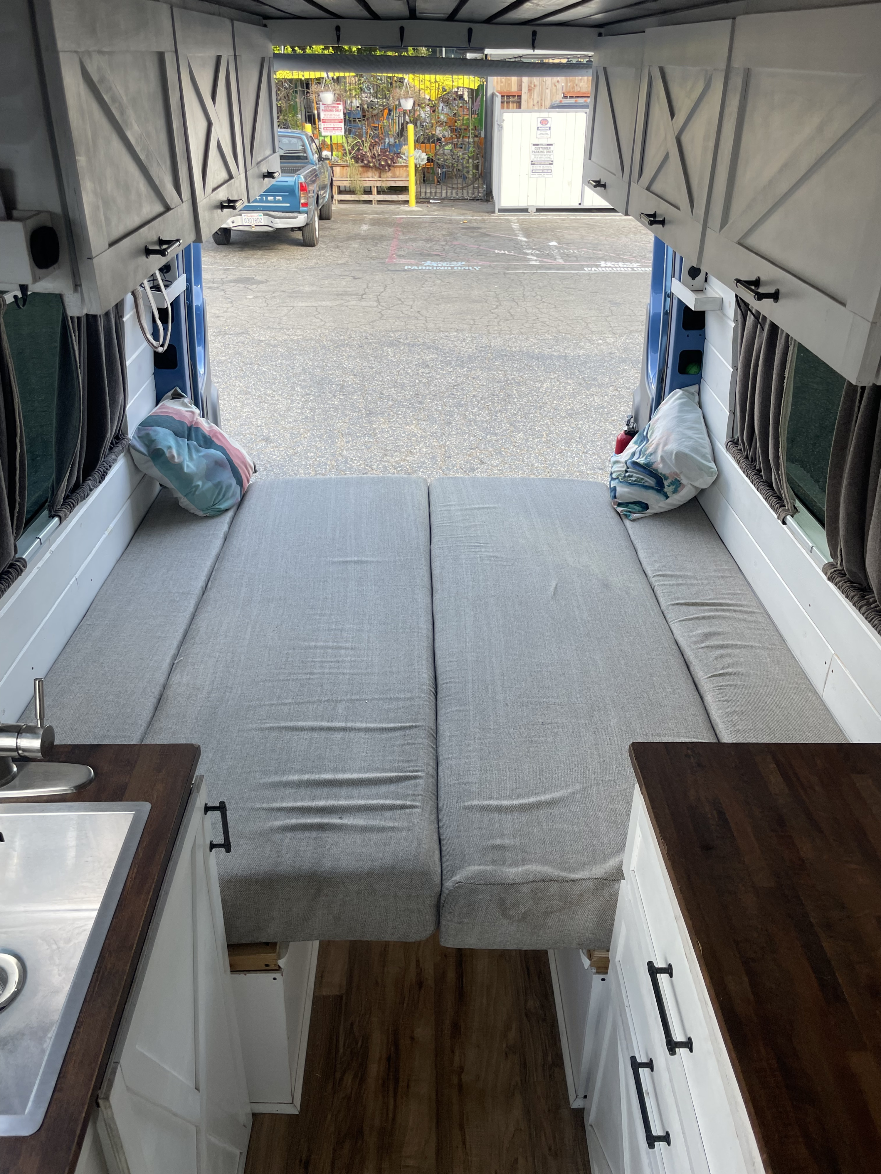 RV rental interior: comfy grey bed, kitchenette, and storage cabinets in a custom camper van. View out back doors.. Mercedes-Benz Sprinter 2008