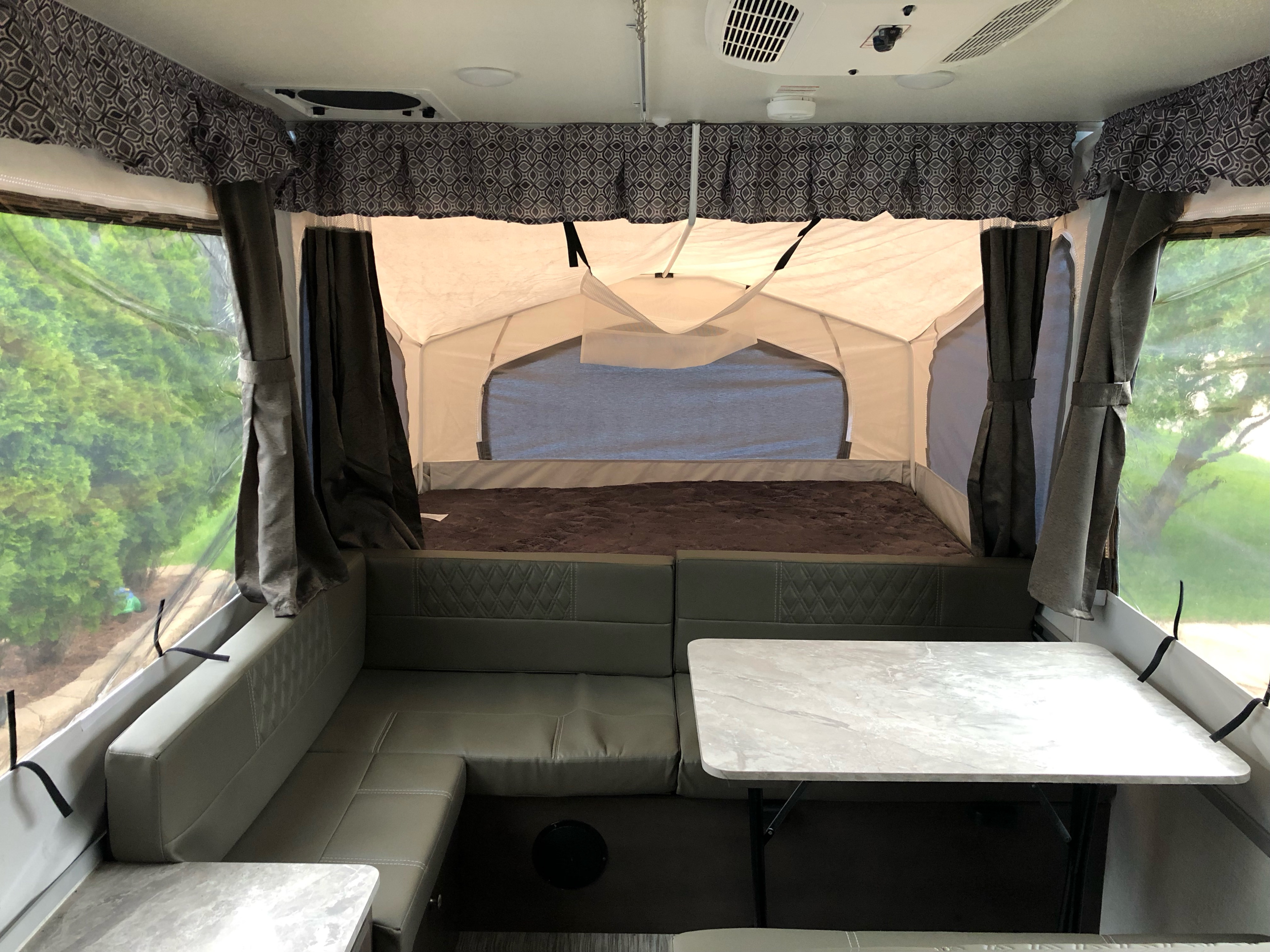 RV rental pop-up camper interior: a cozy bed, U-shaped dinette, and bright windows revealing green trees outside.. Flagstaff Other 2021