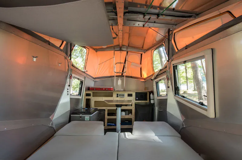 Pop-top RV rental for camping: interior with beds, kitchen, and windows showing a lake view.. TAXA TAXA Trailer 2016