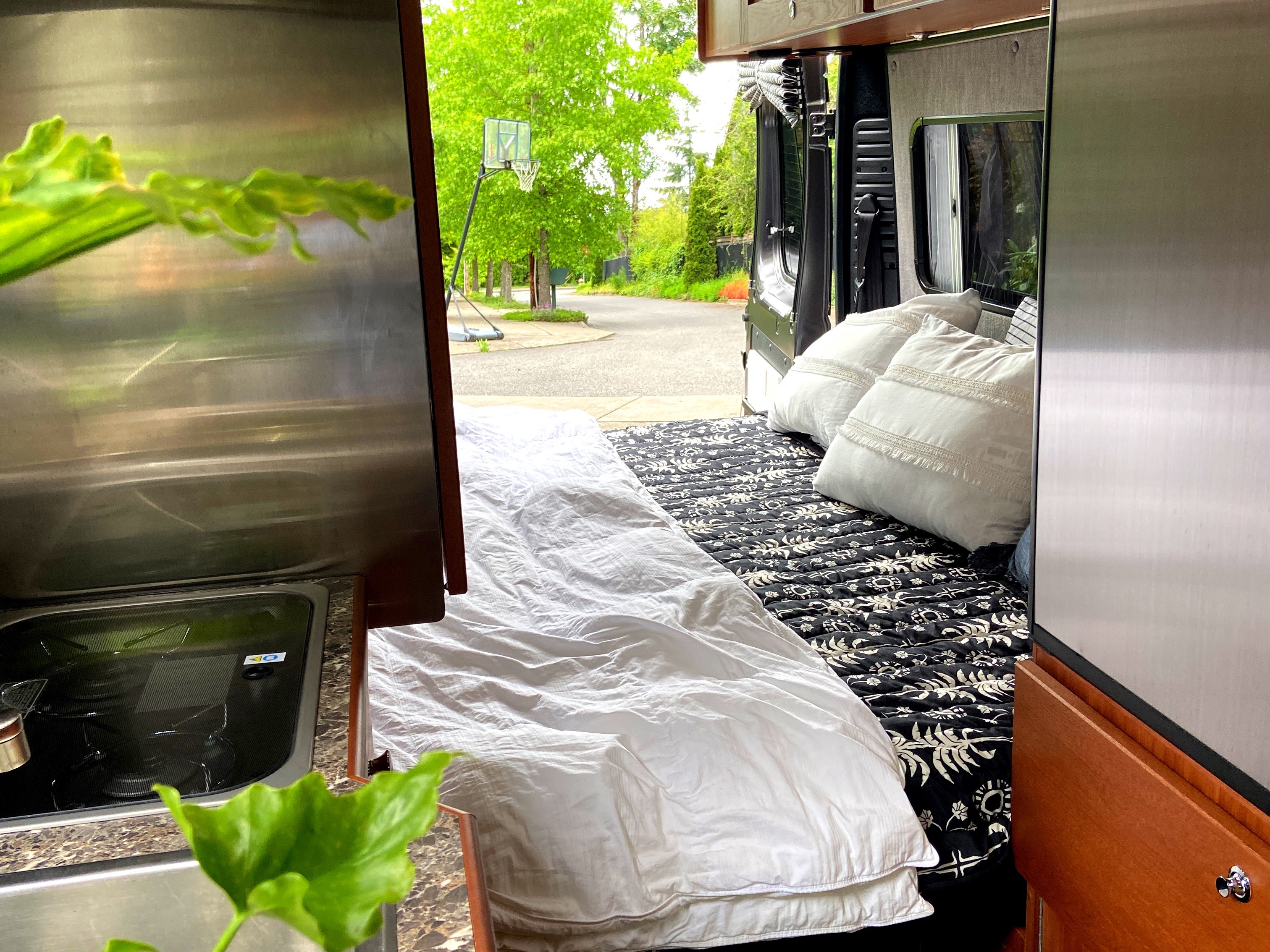 Inside a comfy RV rental: bed, kitchenette, and open door view to a quiet street. Ideal for van life travel.. Roadtrek Roadtrek Class B 2018