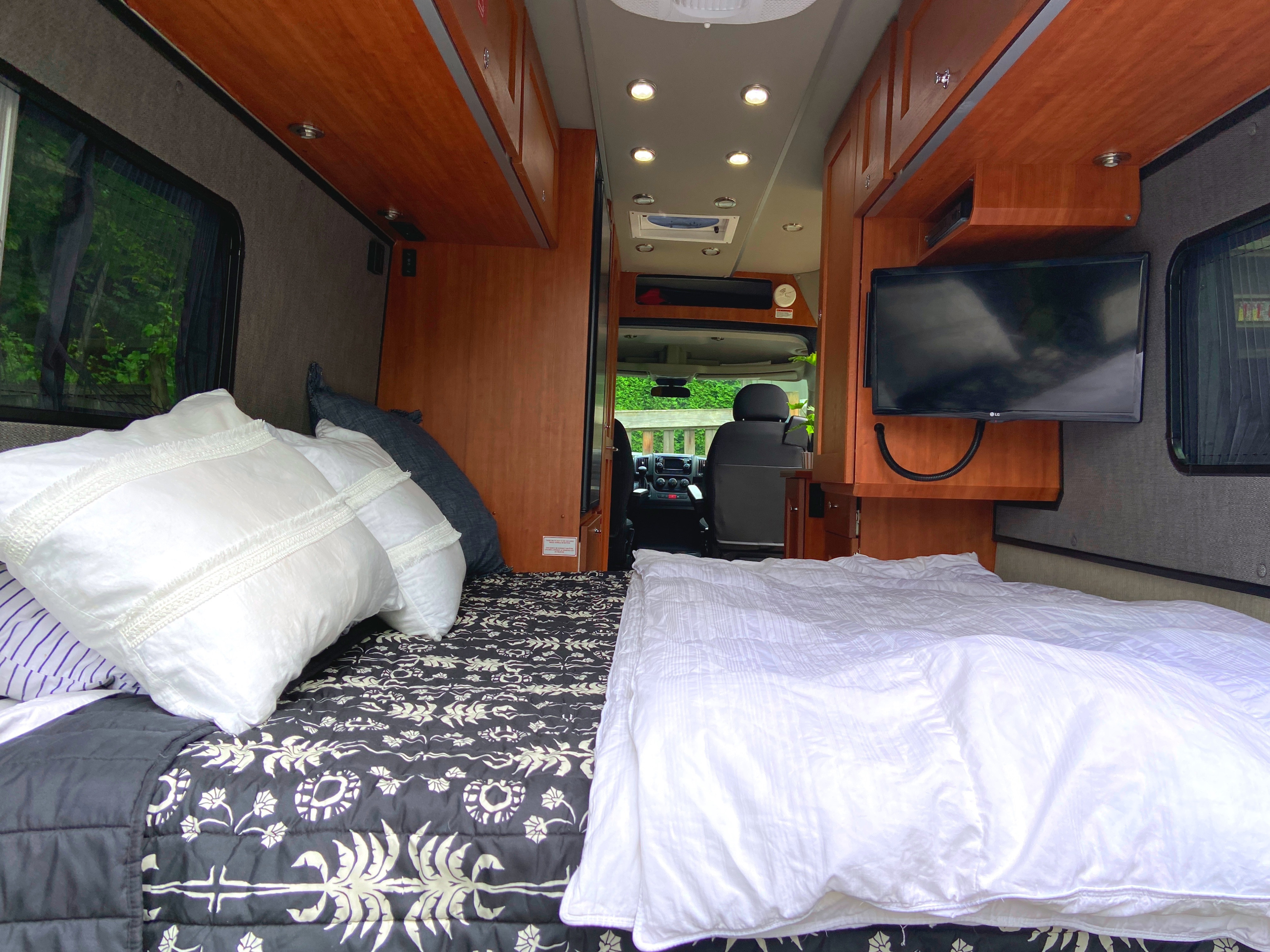 Well-appointed RV rental interior with a comfy bed, white bedding, wooden cabinets, and a TV for your travels.. Roadtrek Roadtrek Class B 2018