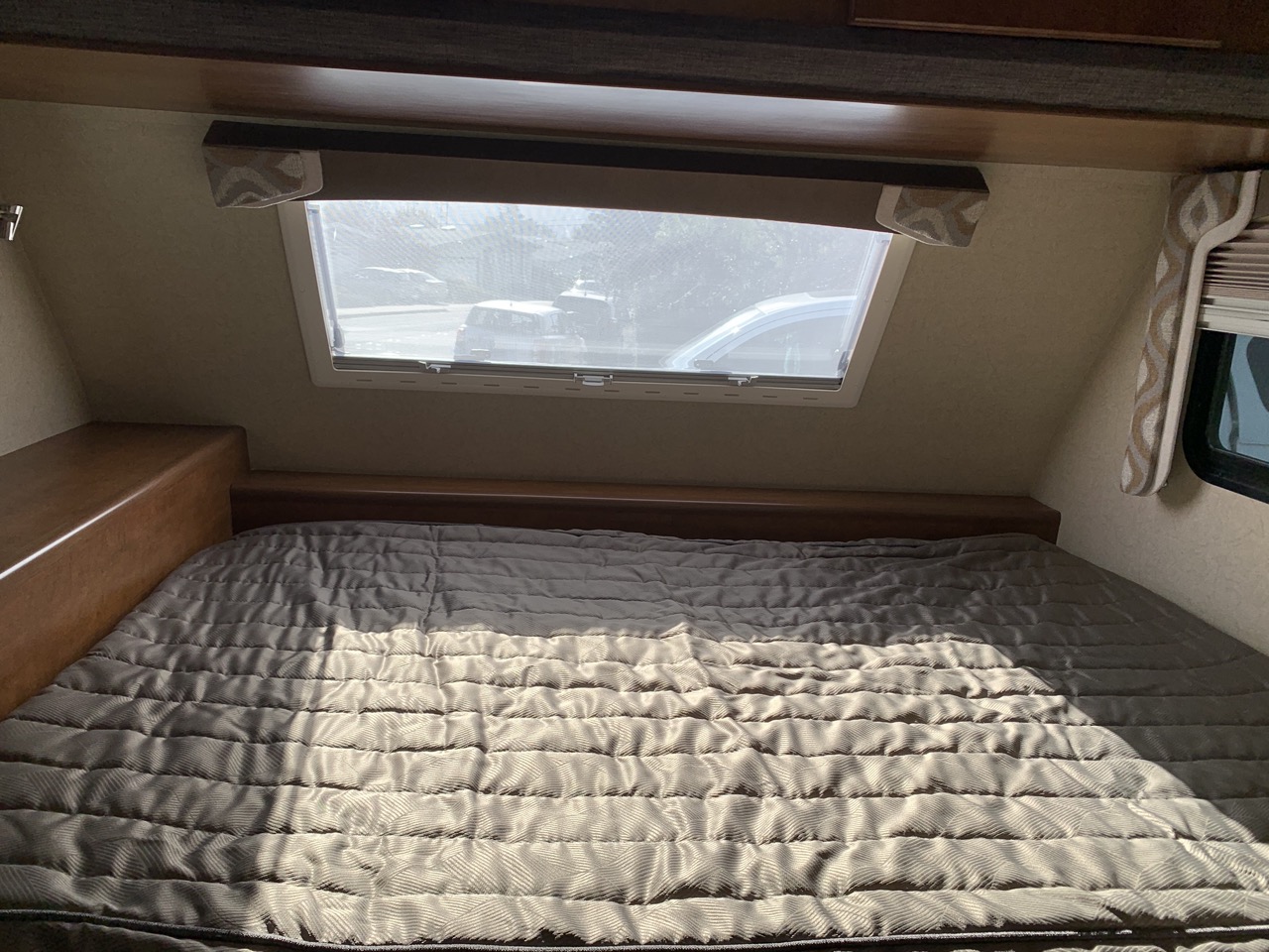 RV rental interior: a comfy bed with a quilted grey comforter, front window, & side shelf.. Lance Manufacturing Lance Manufacturing Trailer 2016