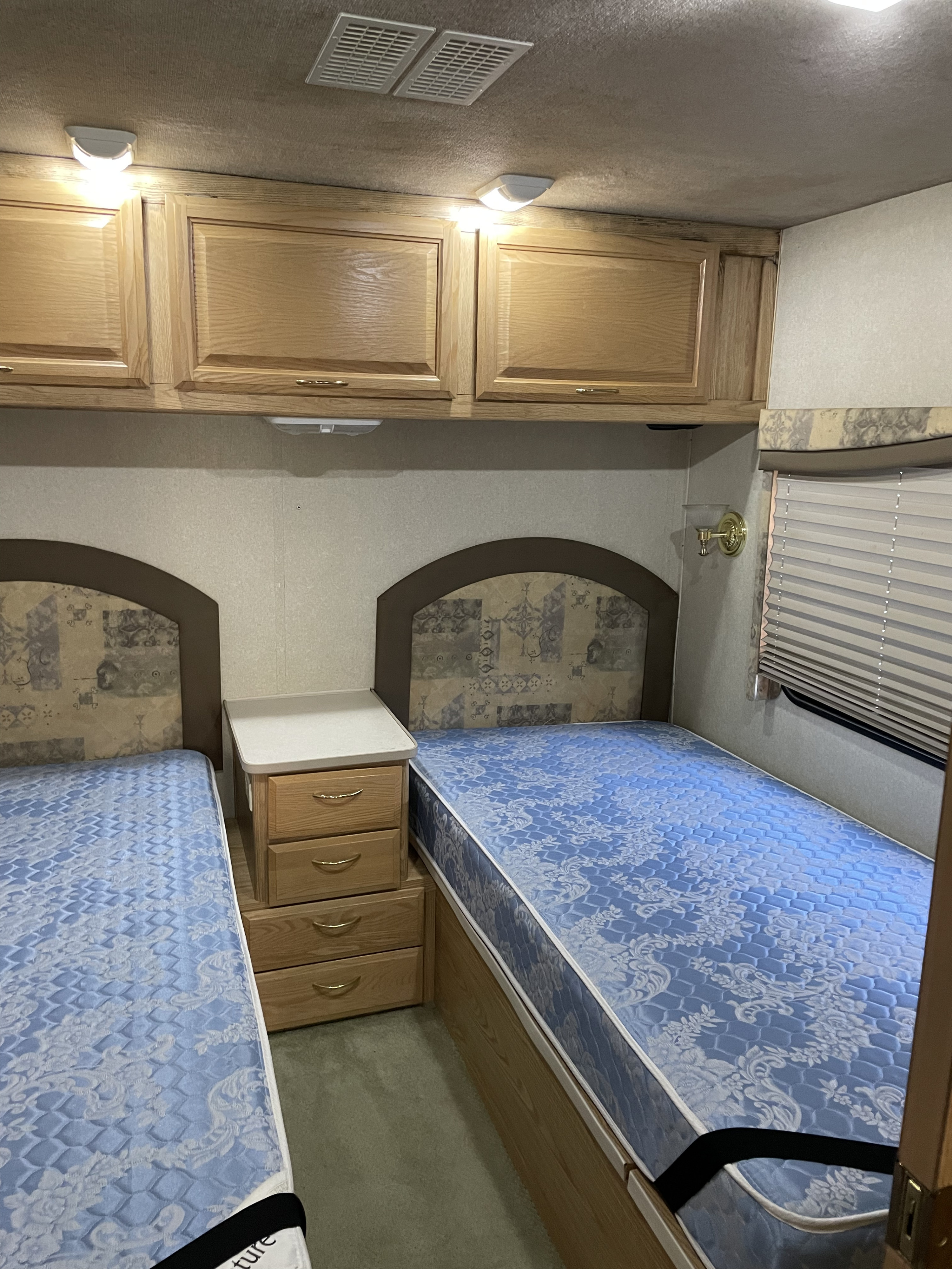RV rental bedroom: two twin beds, a nightstand, and overhead wood cabinets provide compact comfort.. Bounder Bounder Motorhome 2002