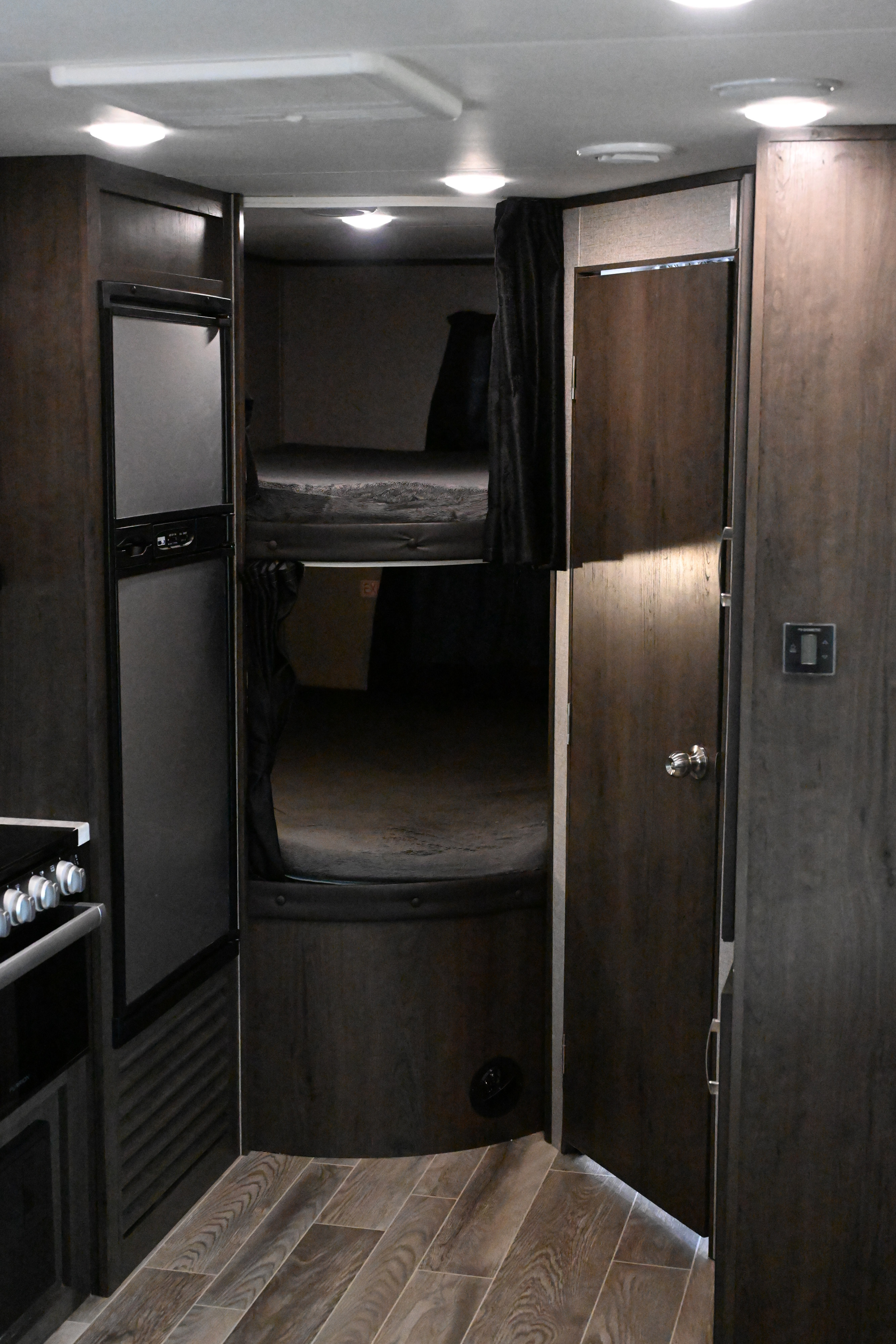 Inside an RV rental: bunk beds with privacy curtains, a refrigerator, and a kitchen area, all with dark wood finishes and light flooring.. Jayco Jay Flight SLX 2021