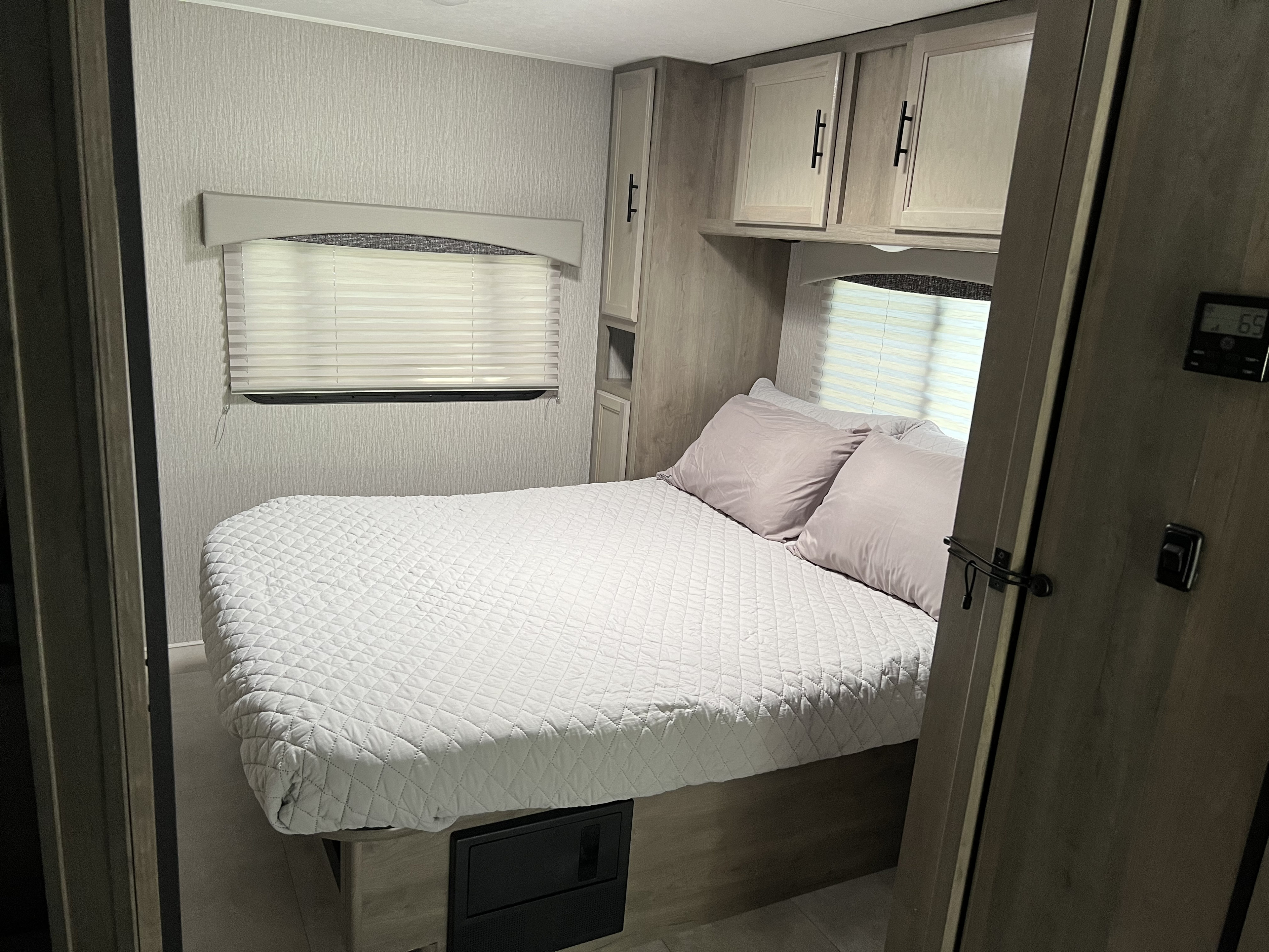 Inside this comfortable RV rental bedroom, find a clean bed, window with blinds, overhead cabinets, and climate controls.. Forest River Coachmen Freelander 2023