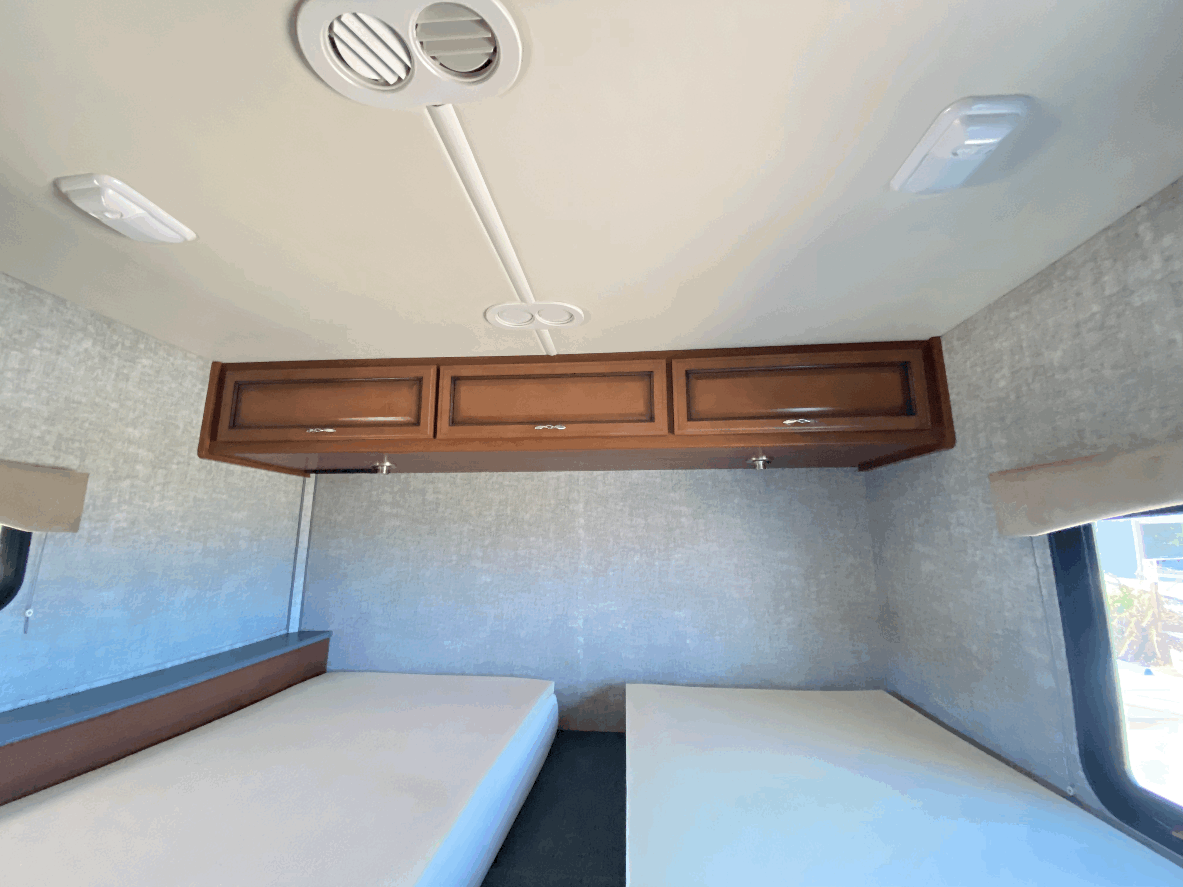 RV rental interior: A clean sleeping area with two mattresses, wood overhead cabinets, and ceiling lights/vents.. Fleetwood Storm 2015