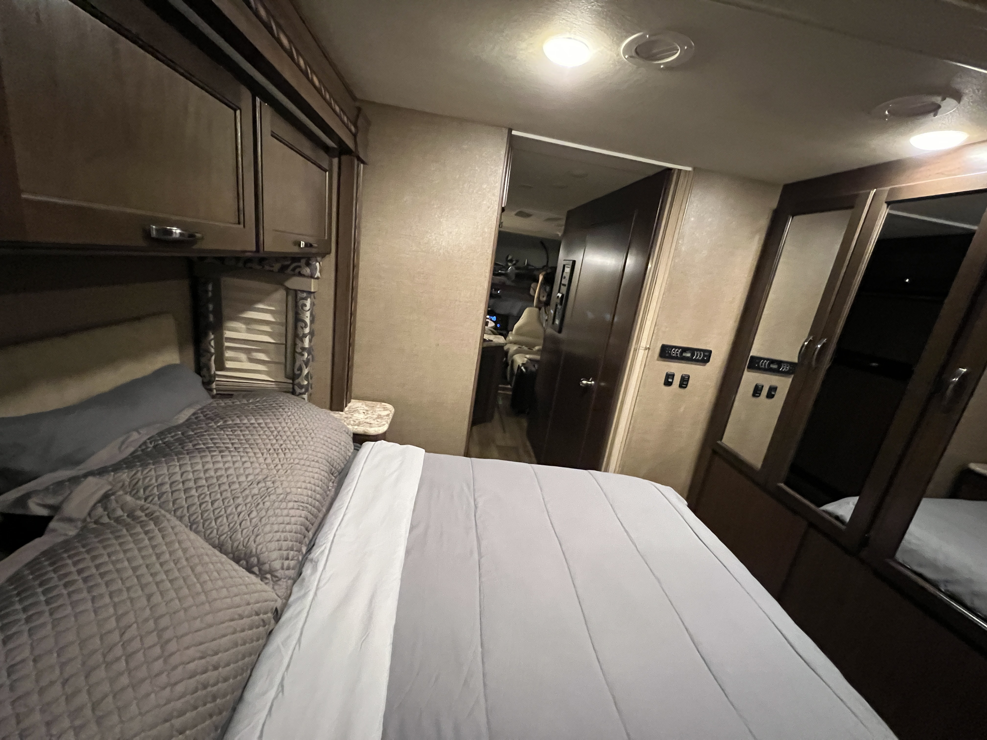 Cozy RV rental bedroom featuring a comfortable bed, overhead cabinets, and mirrored closet, looking into the RV's main area.. Thor Four Winds 2018