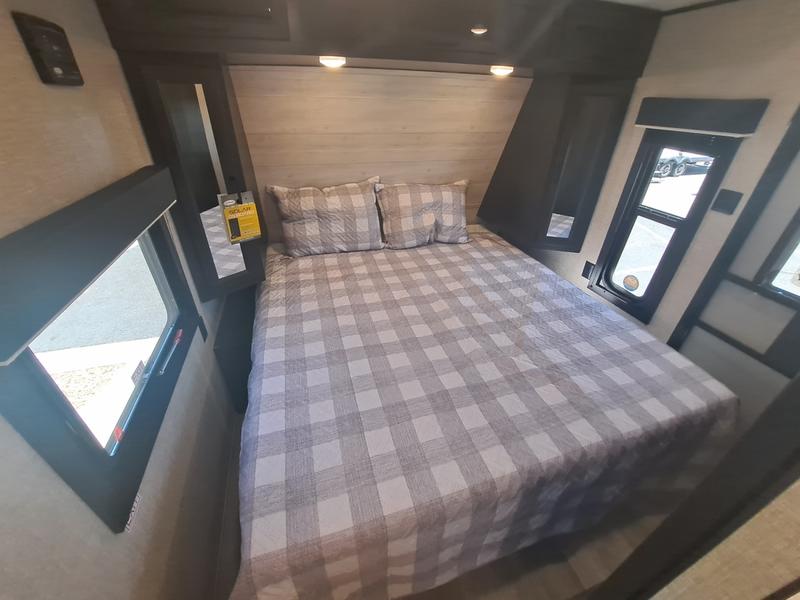 Relax in this RV rental bedroom featuring a comfortable plaid bed, ample windows, and modern dark wood details.. Jayco JayFlight 28BHS TT 2022