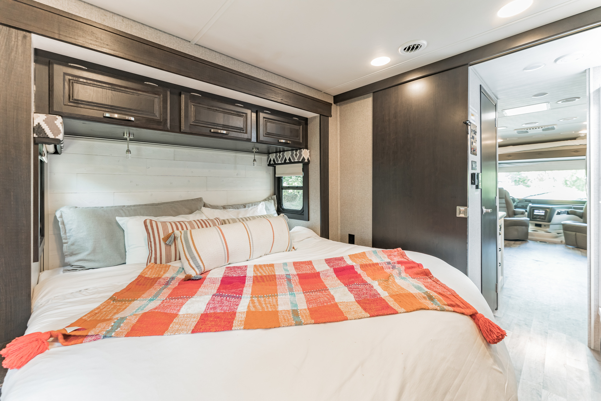 Cozy RV rental bedroom featuring dark wood cabinets, a colorful bed, and a view into the spacious vehicle interior.. Jayco Precept 2021