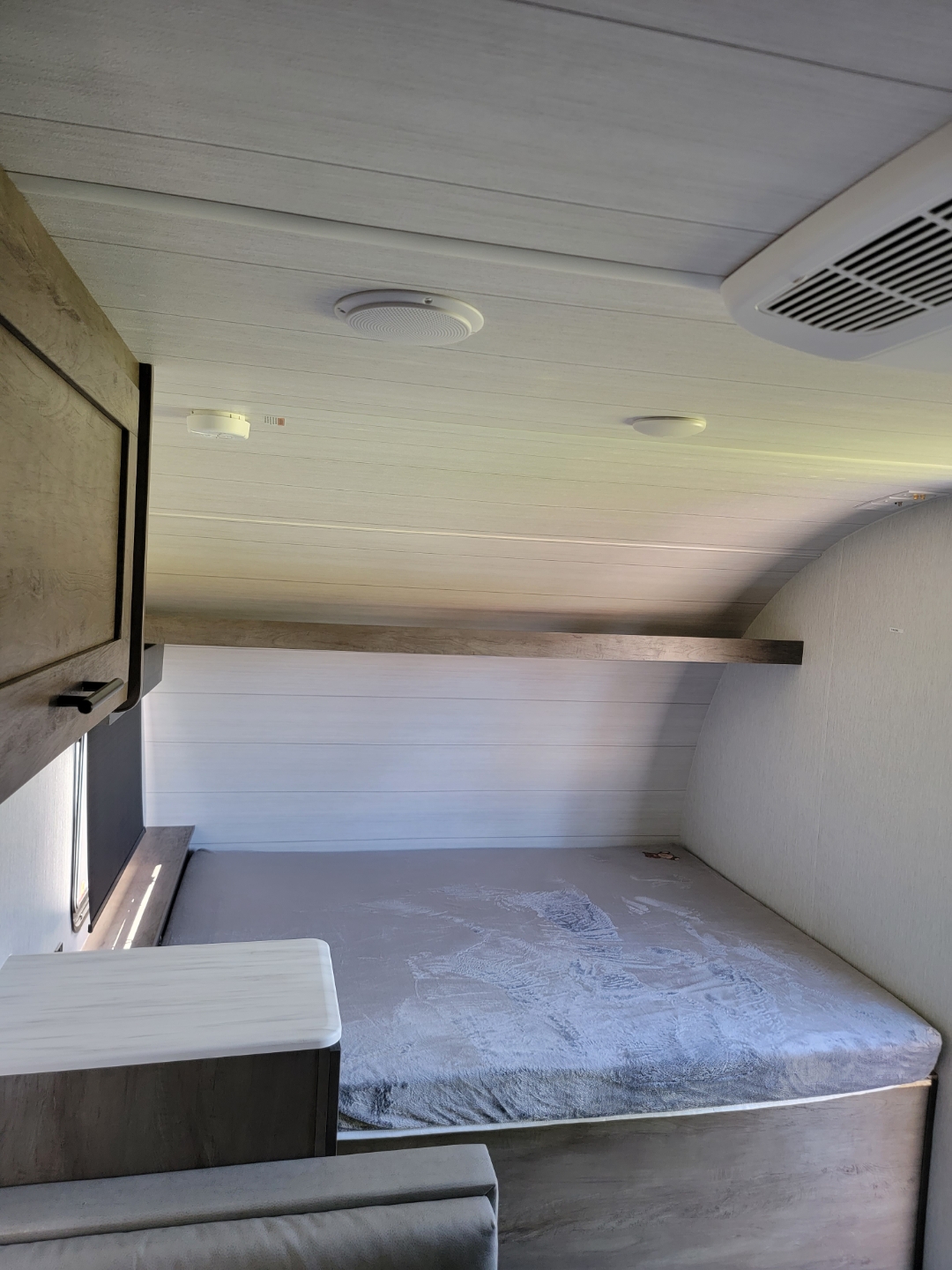 RV rental interior: cozy bedroom with grey mattress, wood-look walls/ceiling, and overhead shelf.. Forest River Salem 2022