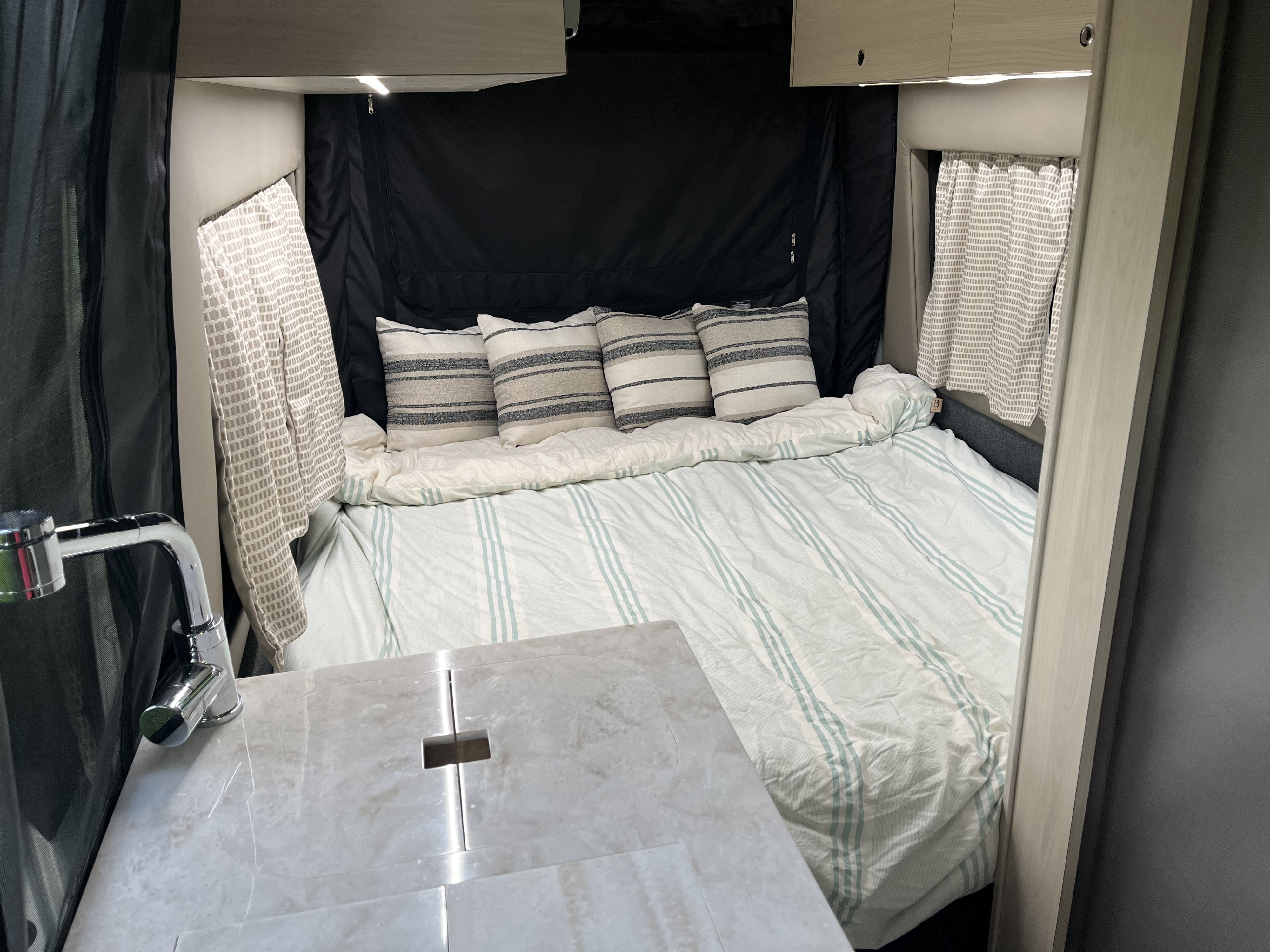 Cozy RV rental interior with a comfy bed, striped bedding, pillows, and a compact kitchen area with a sink. Ideal for travel.. Tiffin Motorhomes Cahaba 2021