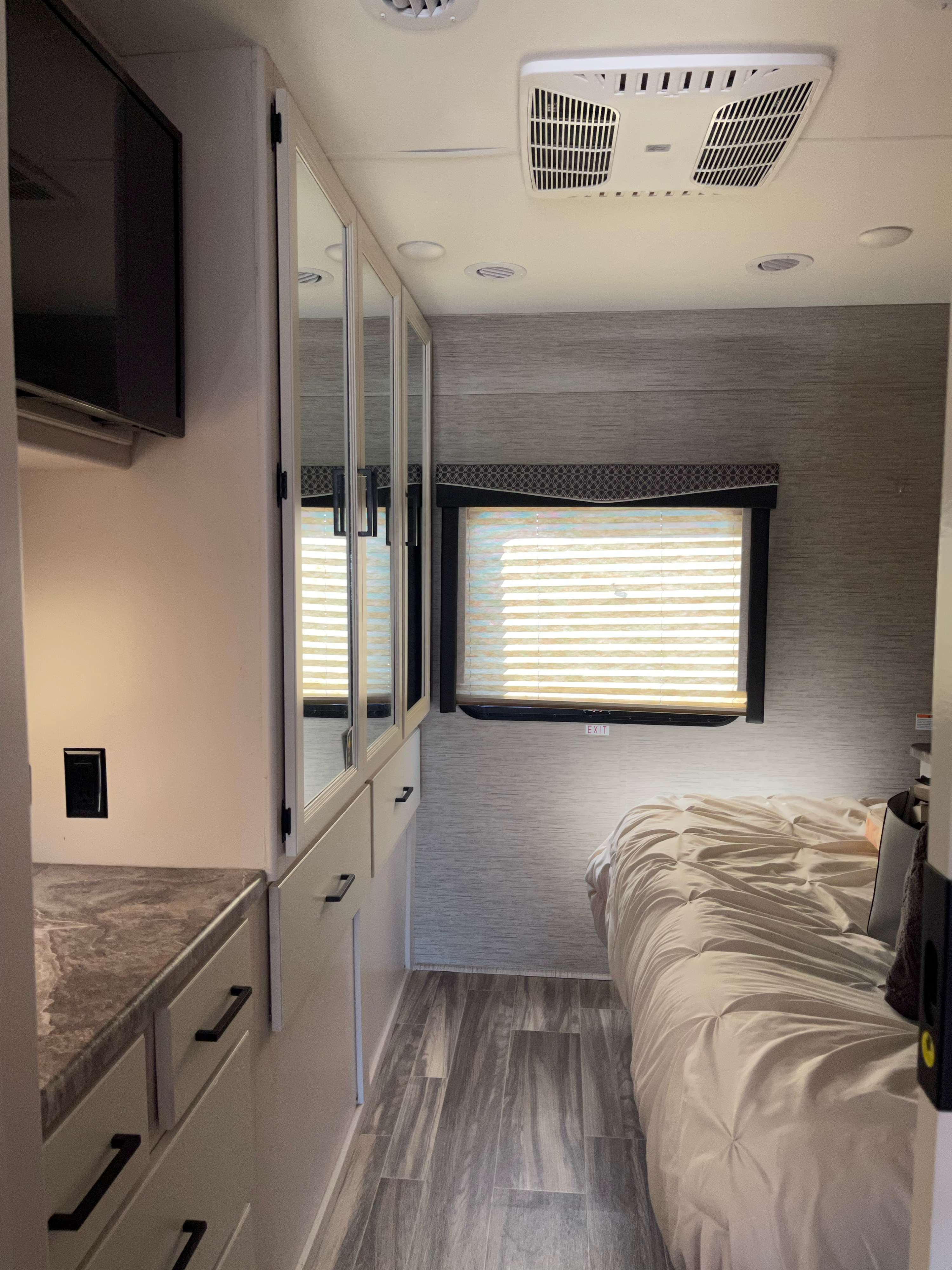 Inside a bright **rv rental** bedroom with a cozy bed, sleek mirrored cabinets, a TV, and AC unit overhead.. Thor A.C.E 2022
