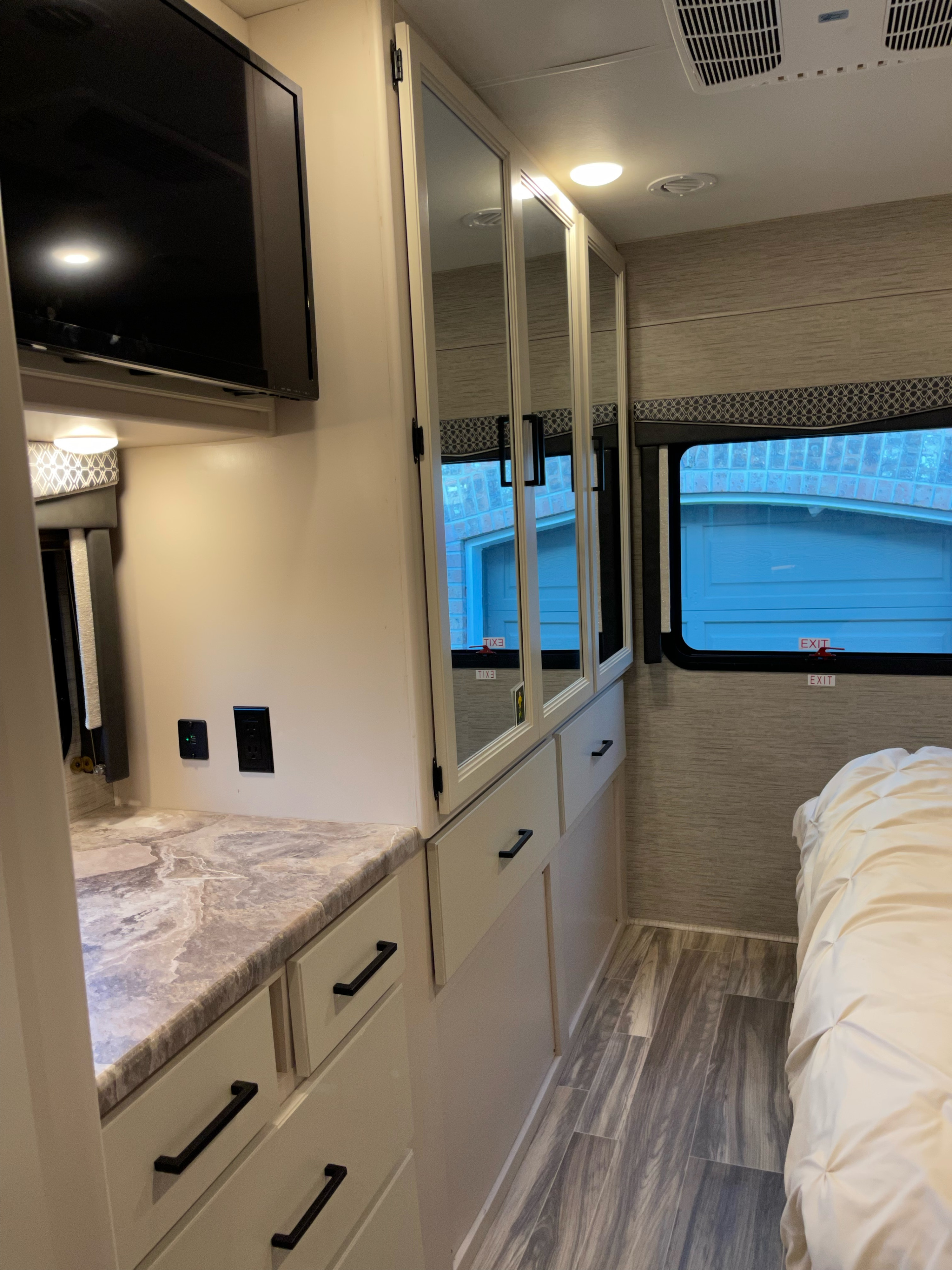 Inside an RV rental: a neat bedroom with TV, mirrored cabinets, counter space, and bed. Modern and functional design.. Thor A.C.E 2022