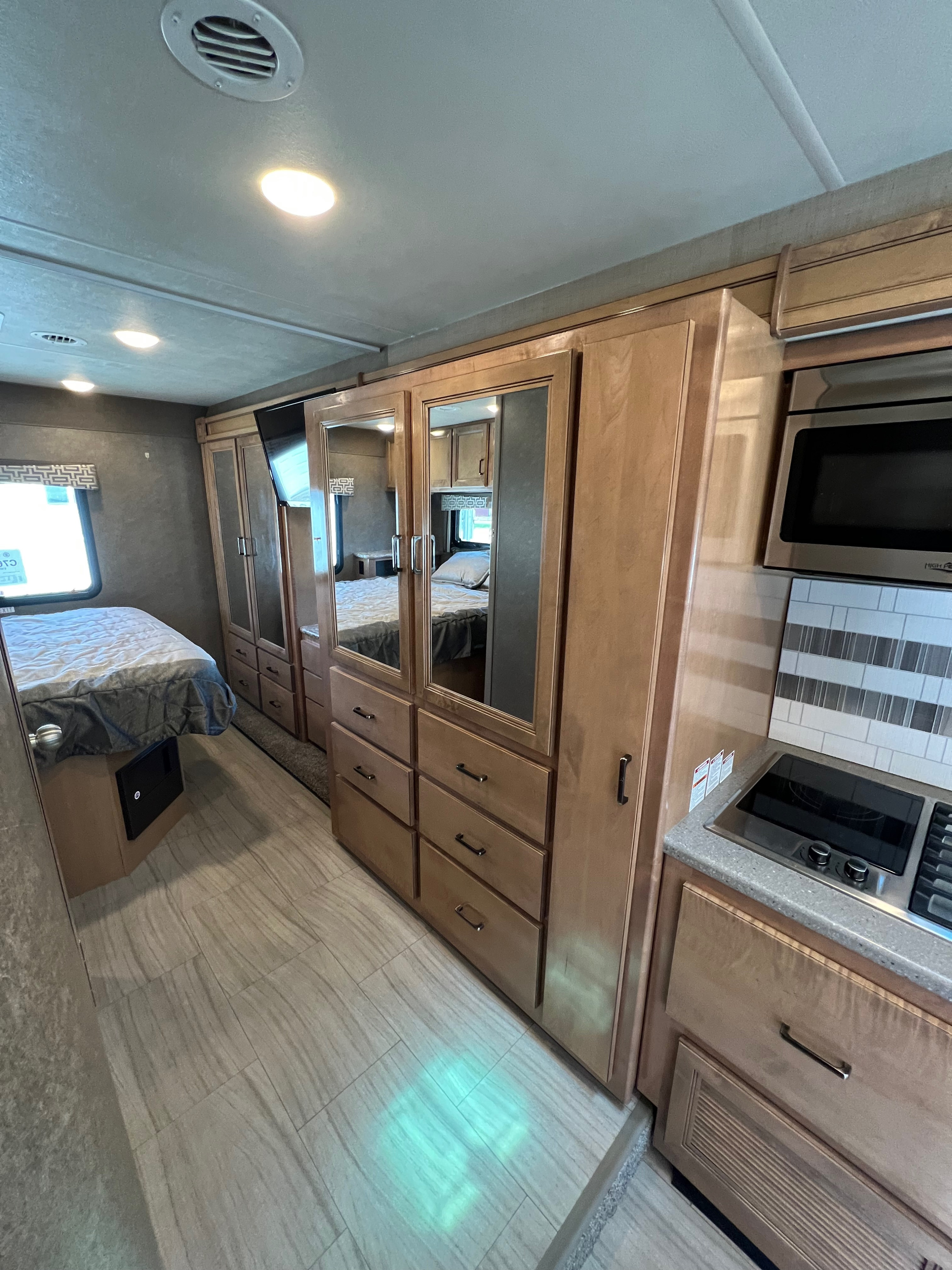 Cozy RV rental interior: bedroom with bed, mirrored wardrobe, and compact kitchen area for comfortable travel.. Thor Quantum 2020