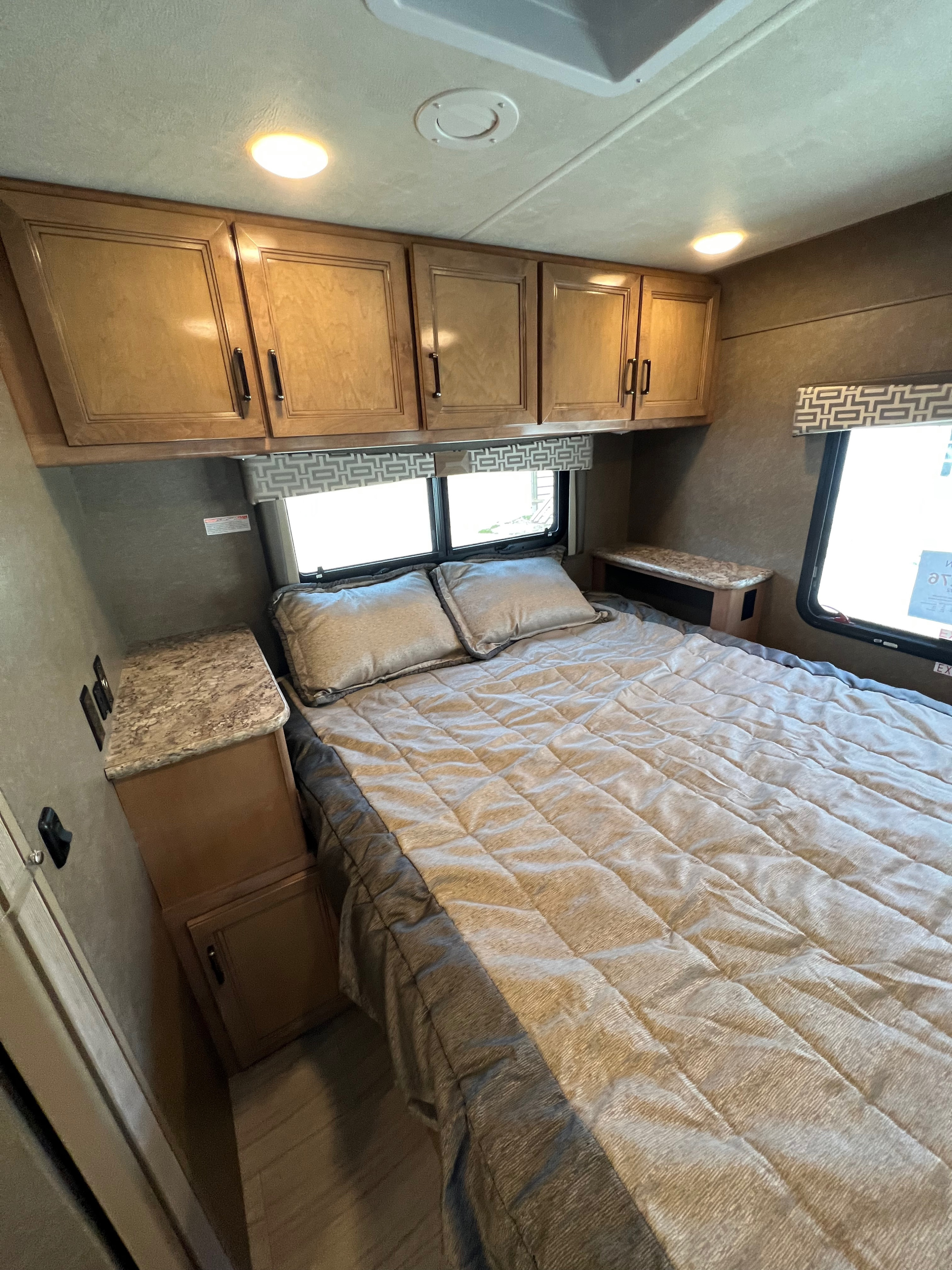 Comfortable RV rental bedroom with light wood overhead cabinets, dual windows, and a cozy bed, designed for travel.. Thor Quantum 2020