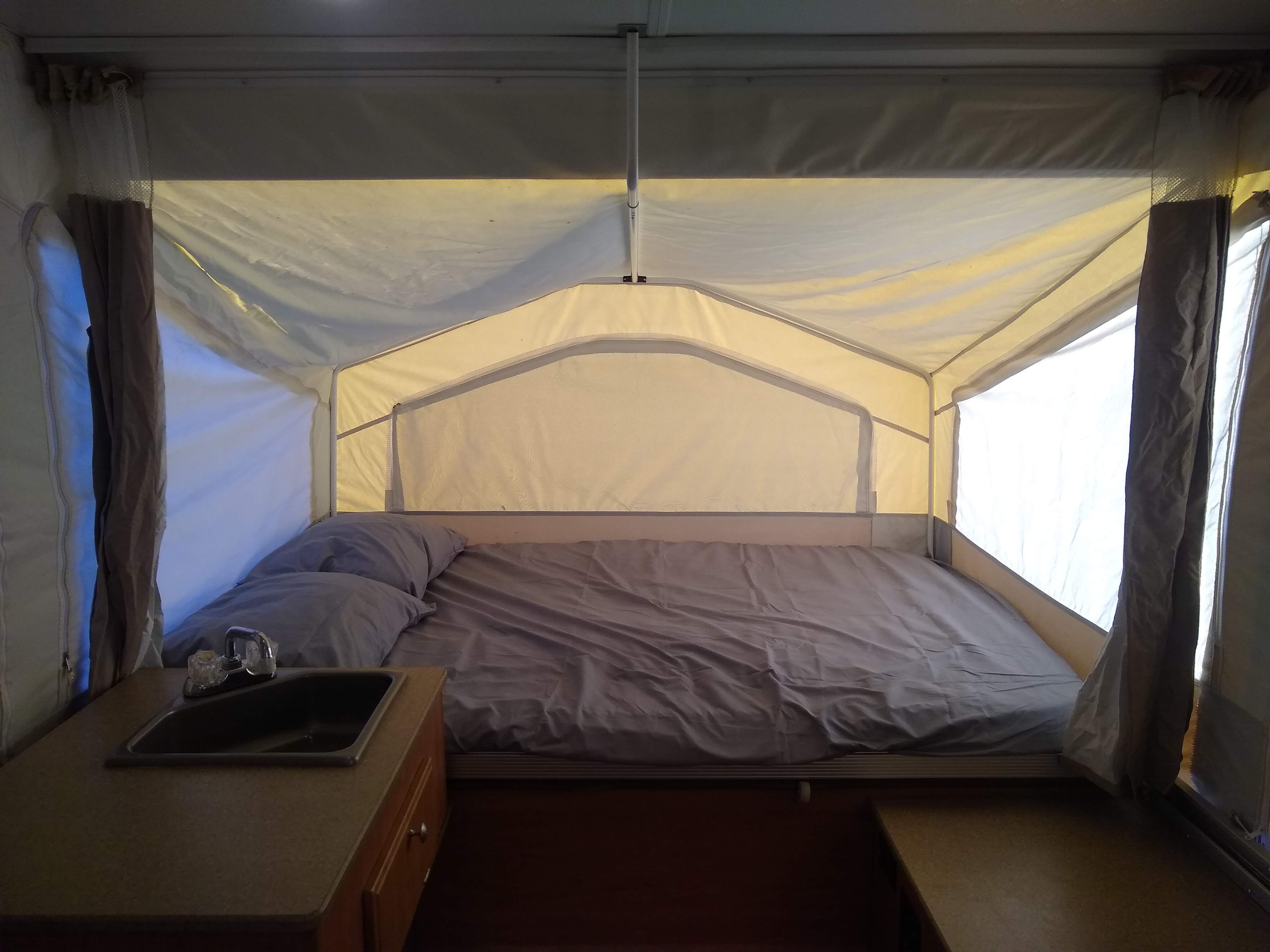 RV rental pop-up camper's interior, showing a comfortable bed with gray linens and pillows, plus a built-in sink.. Forest River Rockwood LTD 2011