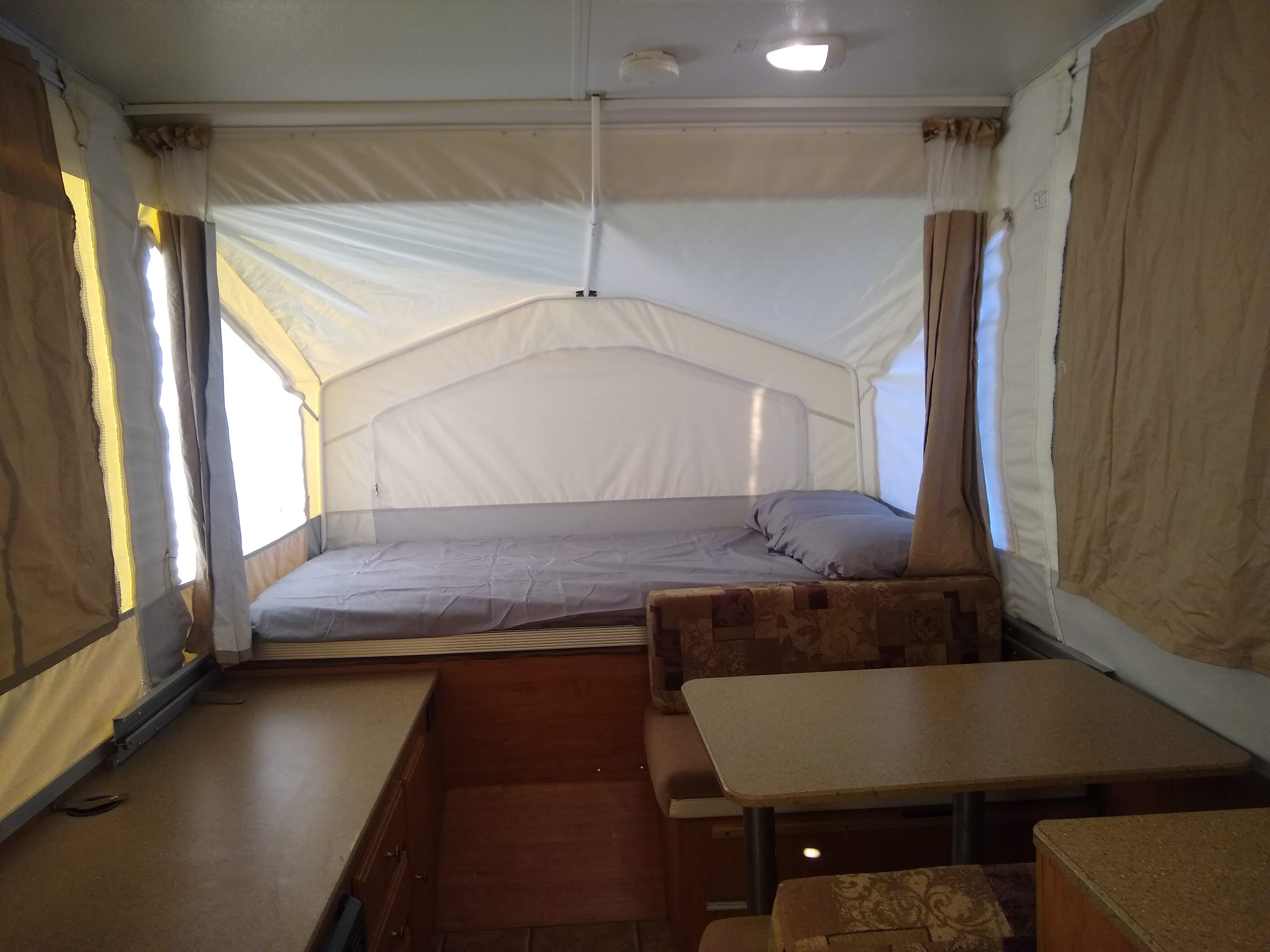 Interior view of a pop-up camper RV rental. Features a comfortable bed, dinette, and storage counter for your travels.. Forest River Rockwood LTD 2011