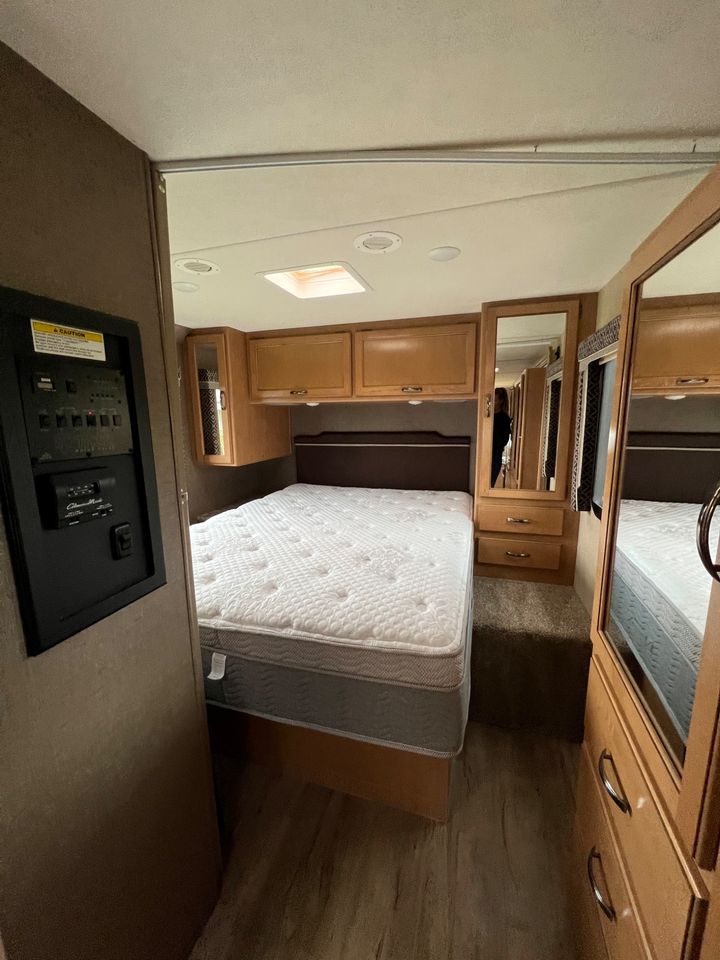 **RV rental** bedroom interior: A cozy space with a white mattress, overhead wood cabinets, and mirrored closets.. Thor Motor Coach Four Winds 2018