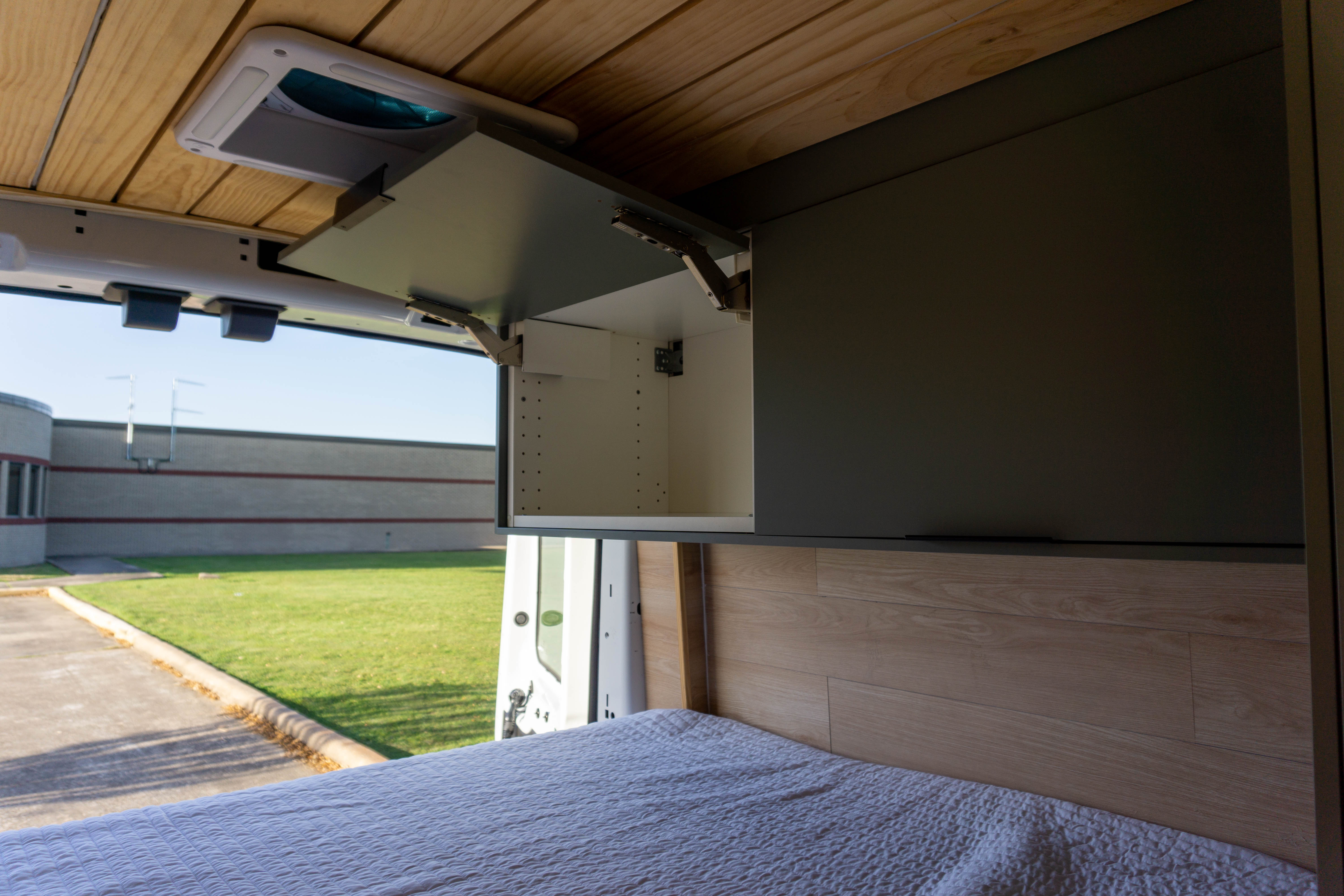 Spacious camper van rv rental interior with wooden ceiling, open overhead cabinet, and comfortable bed with outdoor view.. Ford Transit 2019