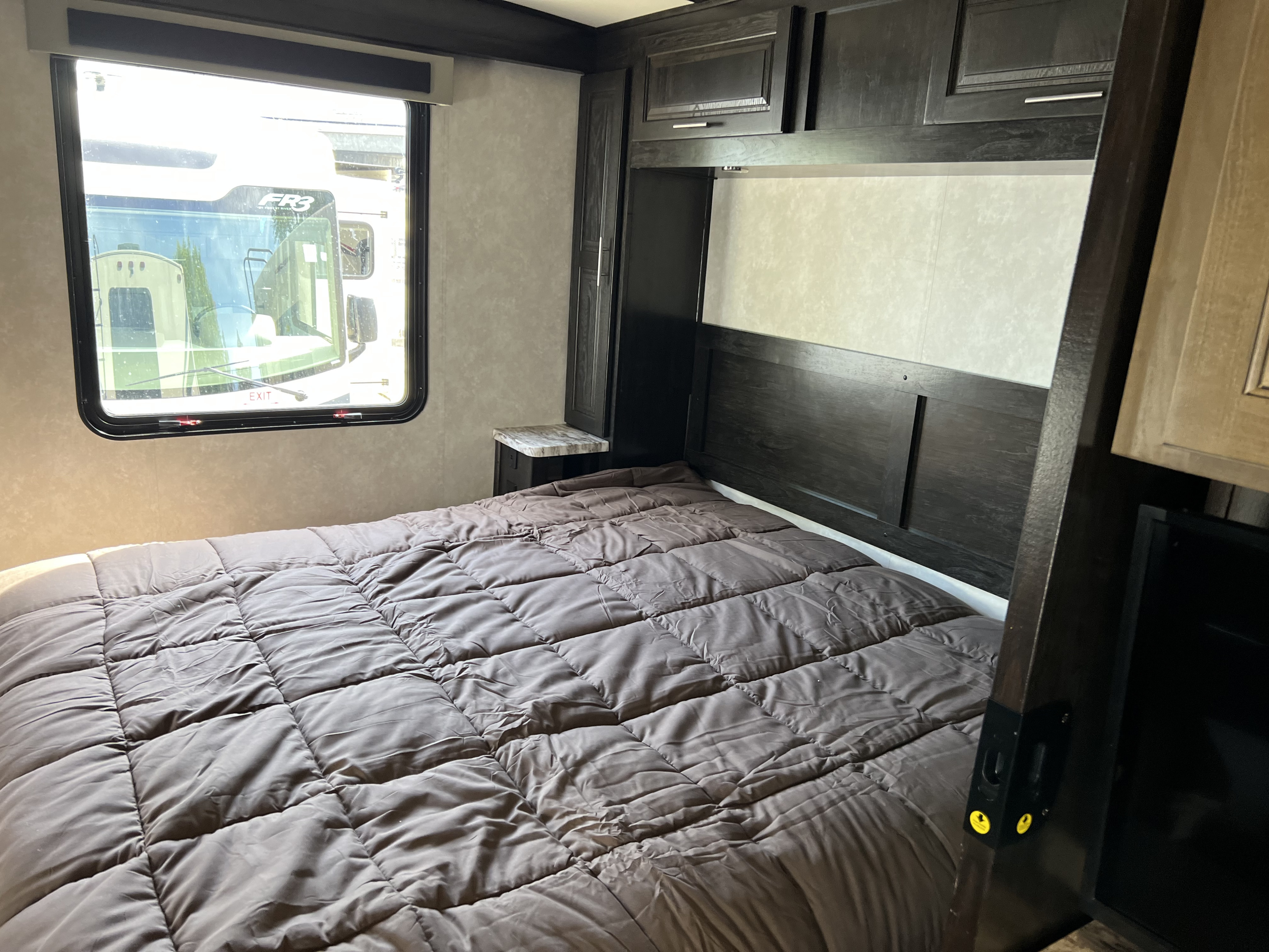 RV rental bedroom featuring a bed with comforter, window showing another RV, dark wood headboard, and nightstand.. Forest River FR3 32DS 2021
