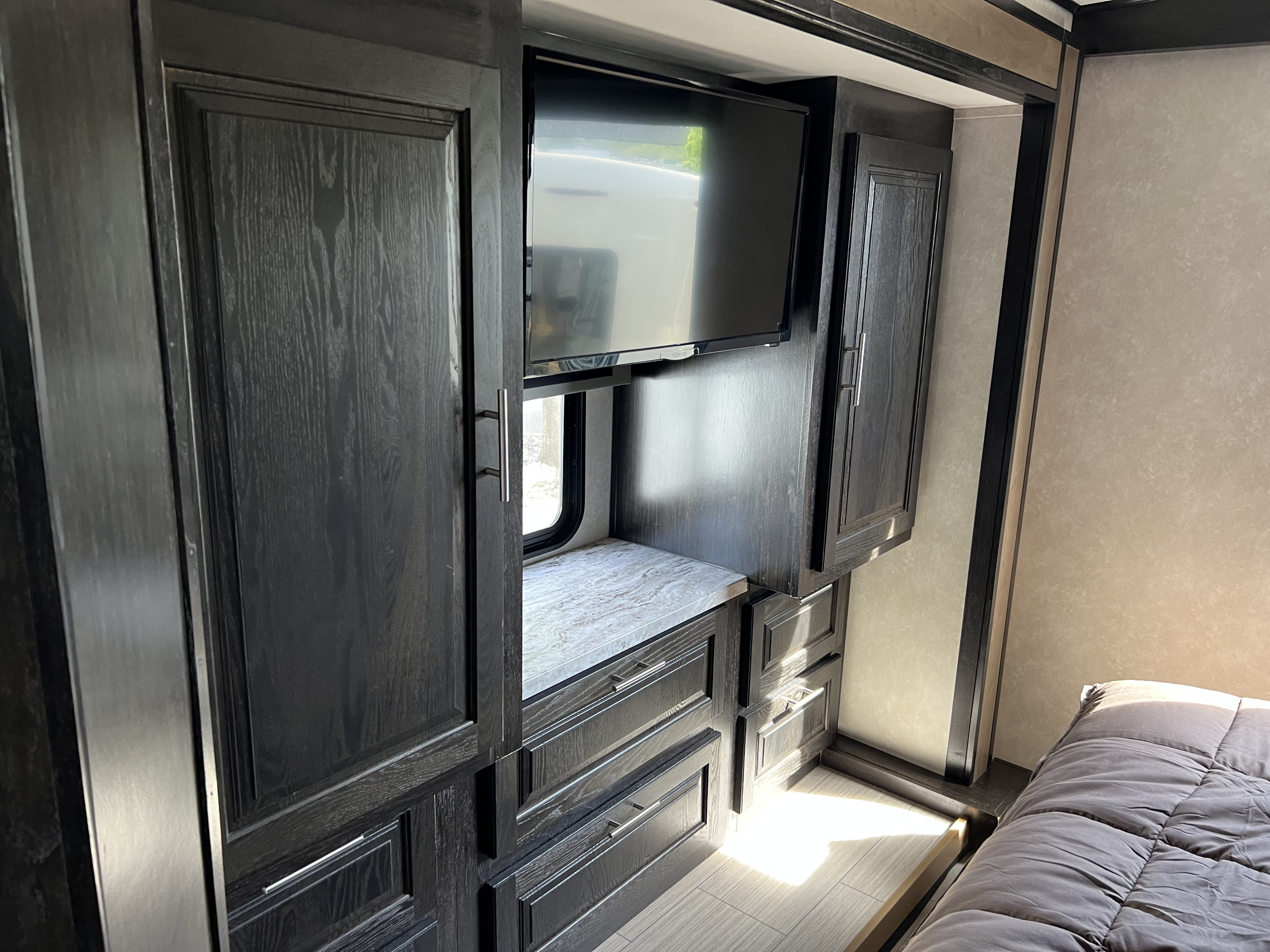 RV rental interior: Modern bedroom featuring dark wood cabinets, mounted TV, window, and smart storage solutions.. Forest River FR3 32DS 2021
