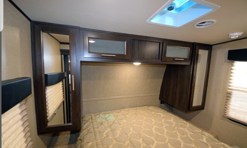 Inside an RV rental, this cozy bedroom features a bed, dark wood overhead cabinets, mirrored wardrobes, and window blinds.. Forest River XLR HyperLite Toy Hauler 2016