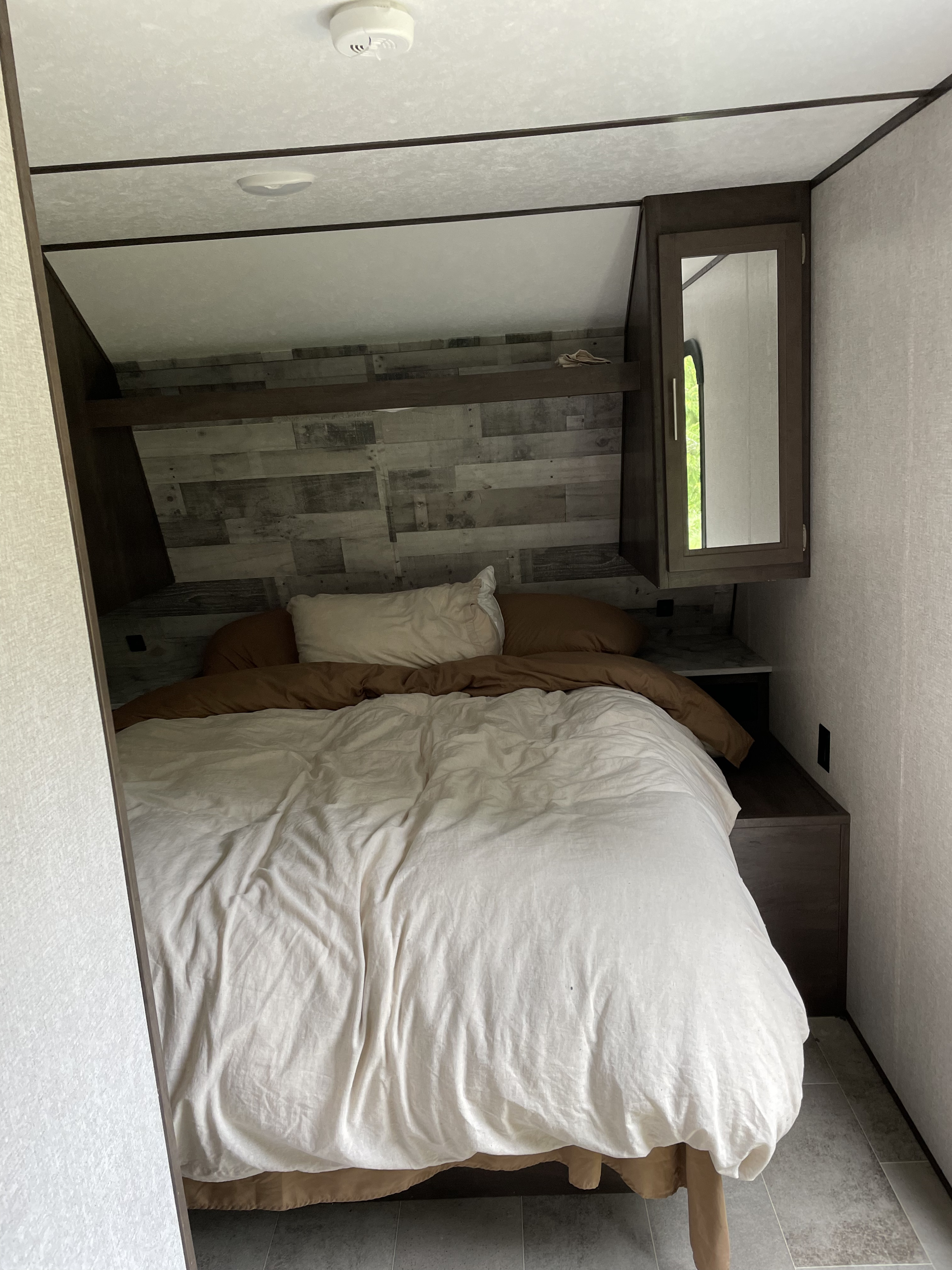 Cozy RV bedroom with a comfortable bed, wood-paneled wall, and mirrored cabinet, ideal for an RV rental.. Coleman Lantern 202RD 2021