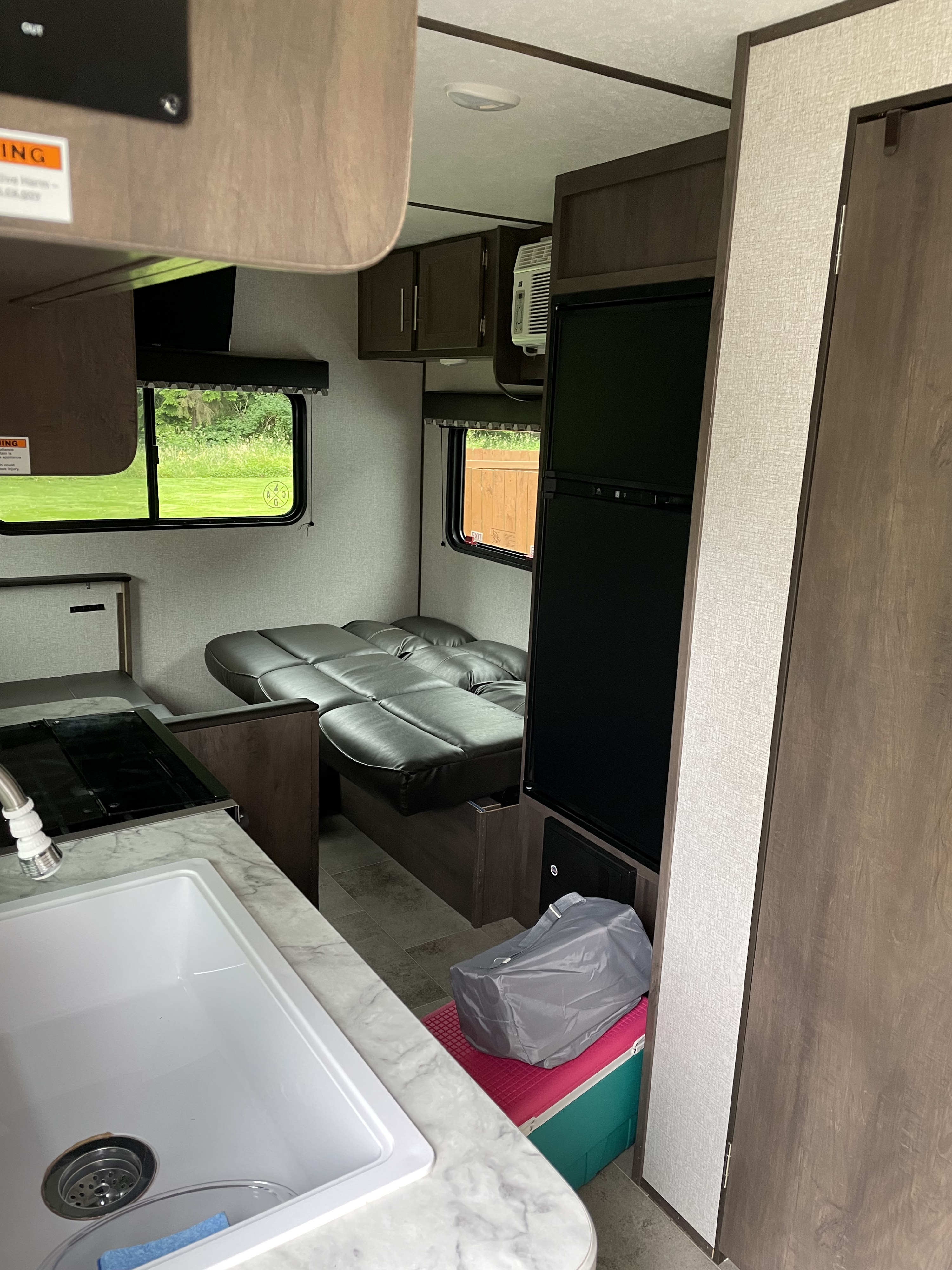 Interior view of a compact RV rental, featuring a kitchen counter with sink/stove, and a convertible dinette/bed.. Coleman Lantern 202RD 2021