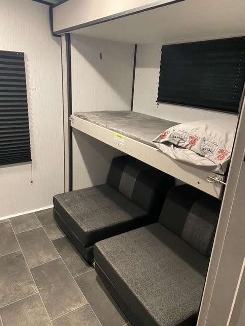 This RV rental interior features bunk beds above dark gray convertible seating, creating a modern, comfortable sleeping and lounge space.. Heartland RVs Mallard 2022