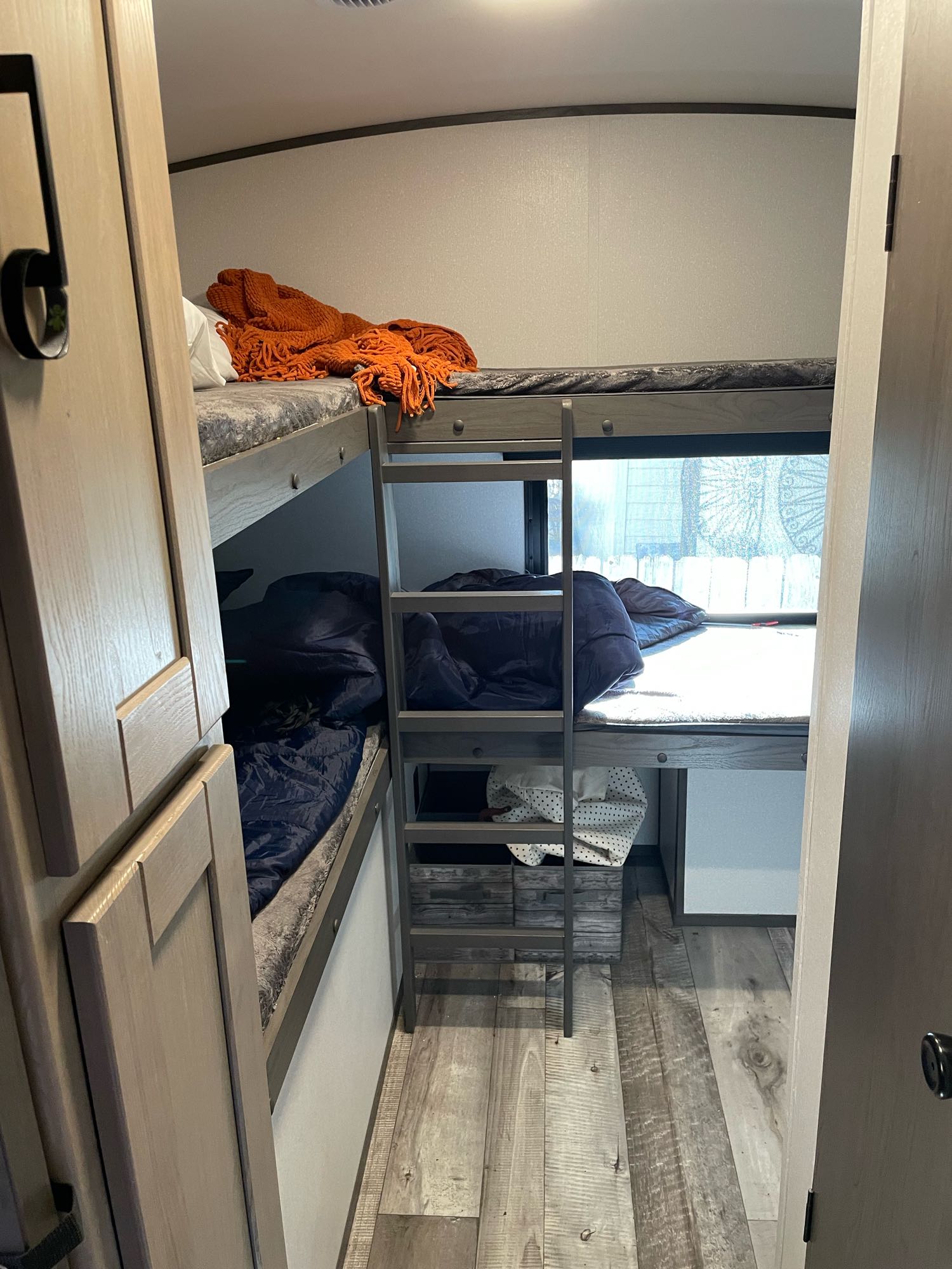 Inside an RV rental: a compact sleeping area with three bunk beds, one with an orange blanket, others with blue sleeping bags.. Heartland RVs Sundance Ultra Lite 2022
