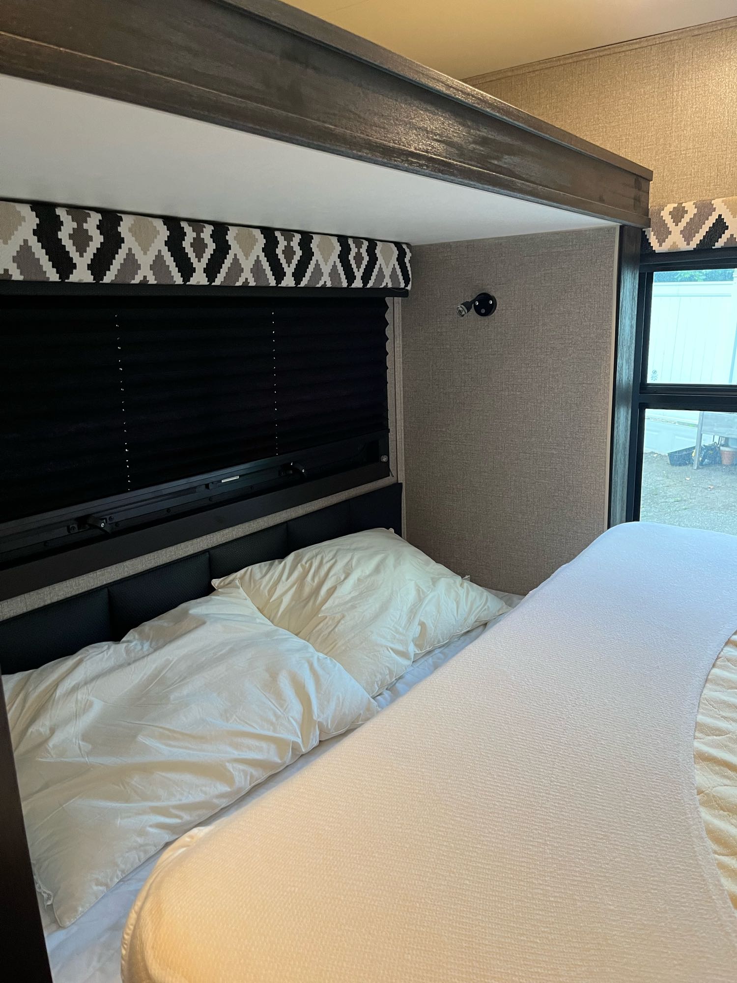 RV rental bedroom with white bedding, black window shades, and a decorative patterned valance.. Entegra Coach Odyssey 2021