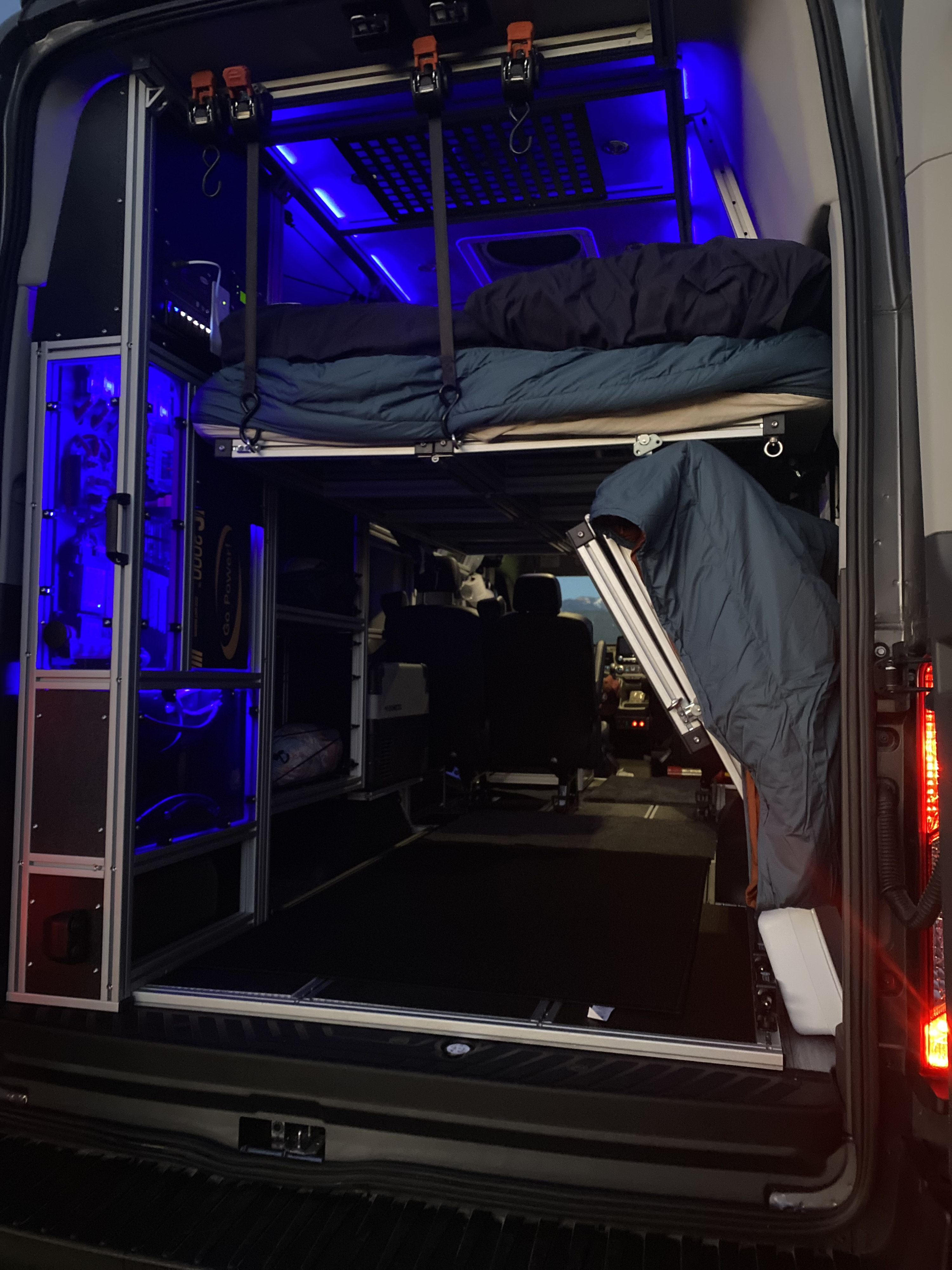 Modern camper van interior with blue-lit tech, elevated bed, and ample storage for your RV rental.. Ford Transit Custom 2021
