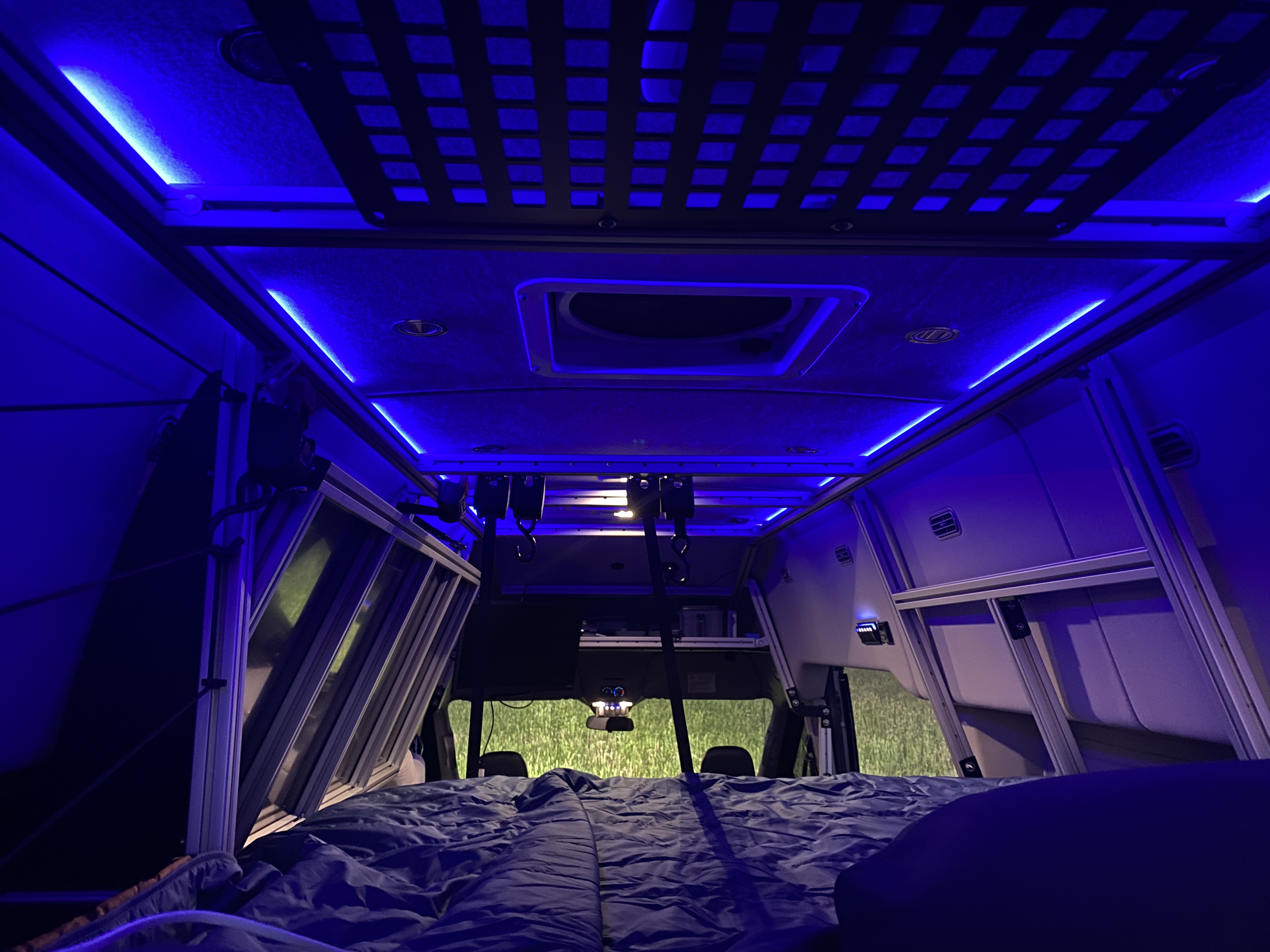 Cozy RV rental interior at night: blue LED lighting, overhead storage, and comfy bed for peaceful travels.. Ford Transit Custom 2021