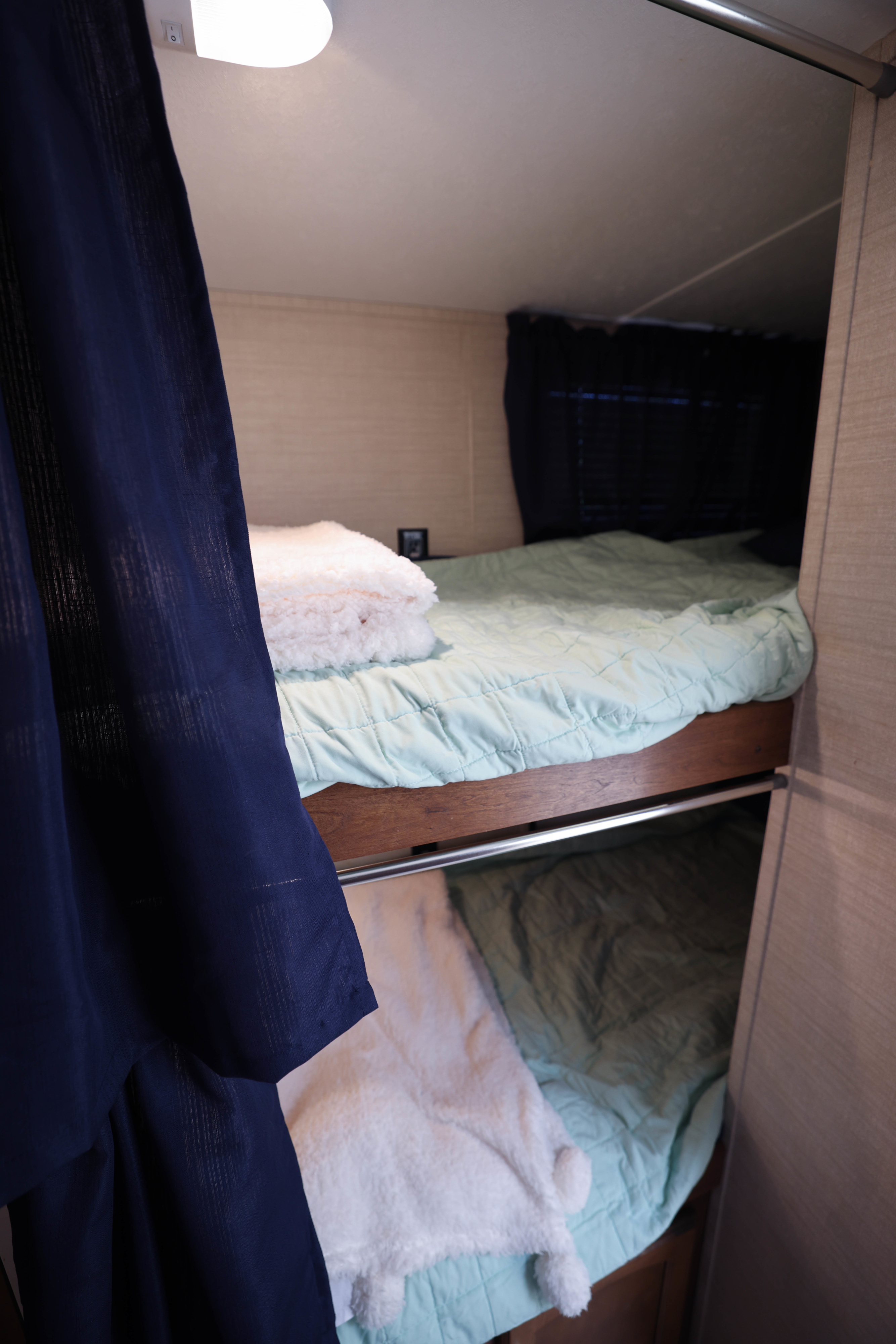 Cozy bunk beds inside this RV rental, featuring mint green quilts and fluffy white blankets, ready for comfortable travel.. Keystone RV Summerland 2016