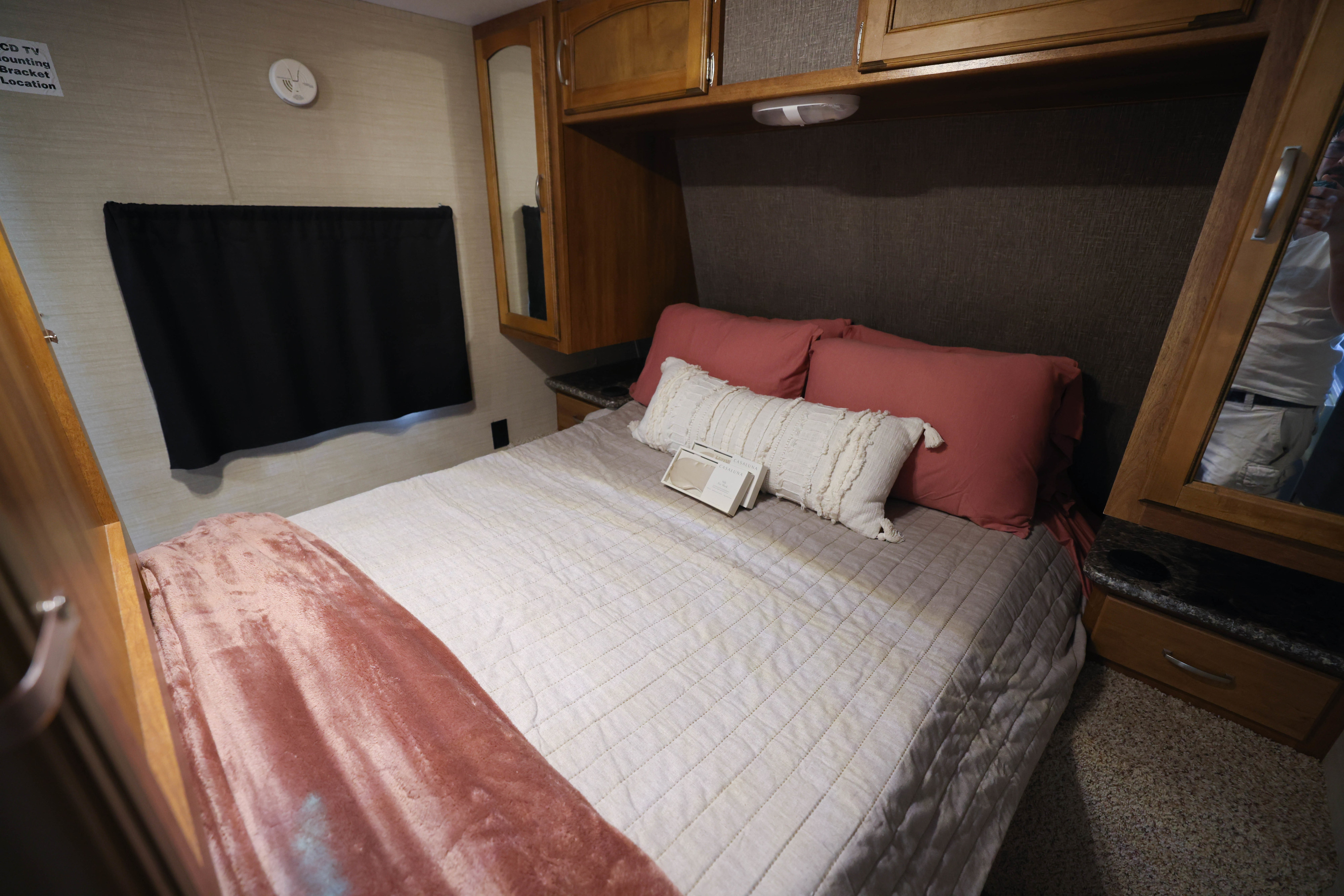 Cozy RV rental bedroom featuring a comfortable bed with a white quilted comforter, pink pillows, and wood cabinets.. Keystone RV Summerland 2016