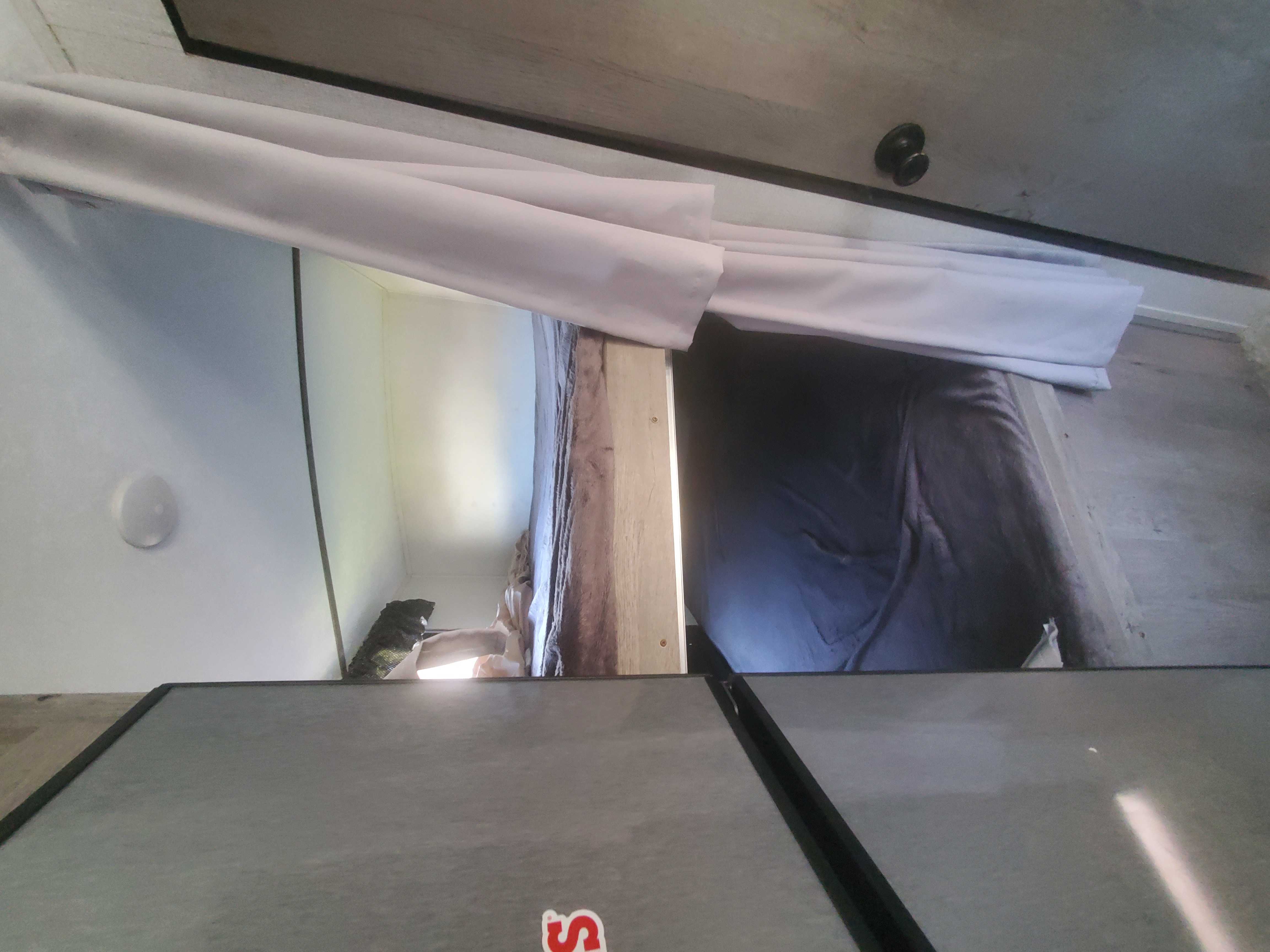 An RV rental's cozy sleeping area features a bed with dark bedding, partly covered by a white privacy curtain.. Keystone Springdale 2021