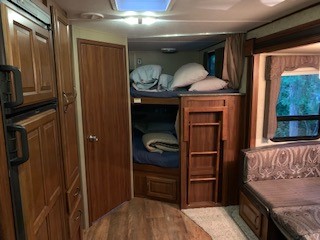Inside an RV rental: a cozy bunk bed nook with ladder, a compact kitchen on the left, and a dinette with a window on the right.. Keystone RV Cougar 2014