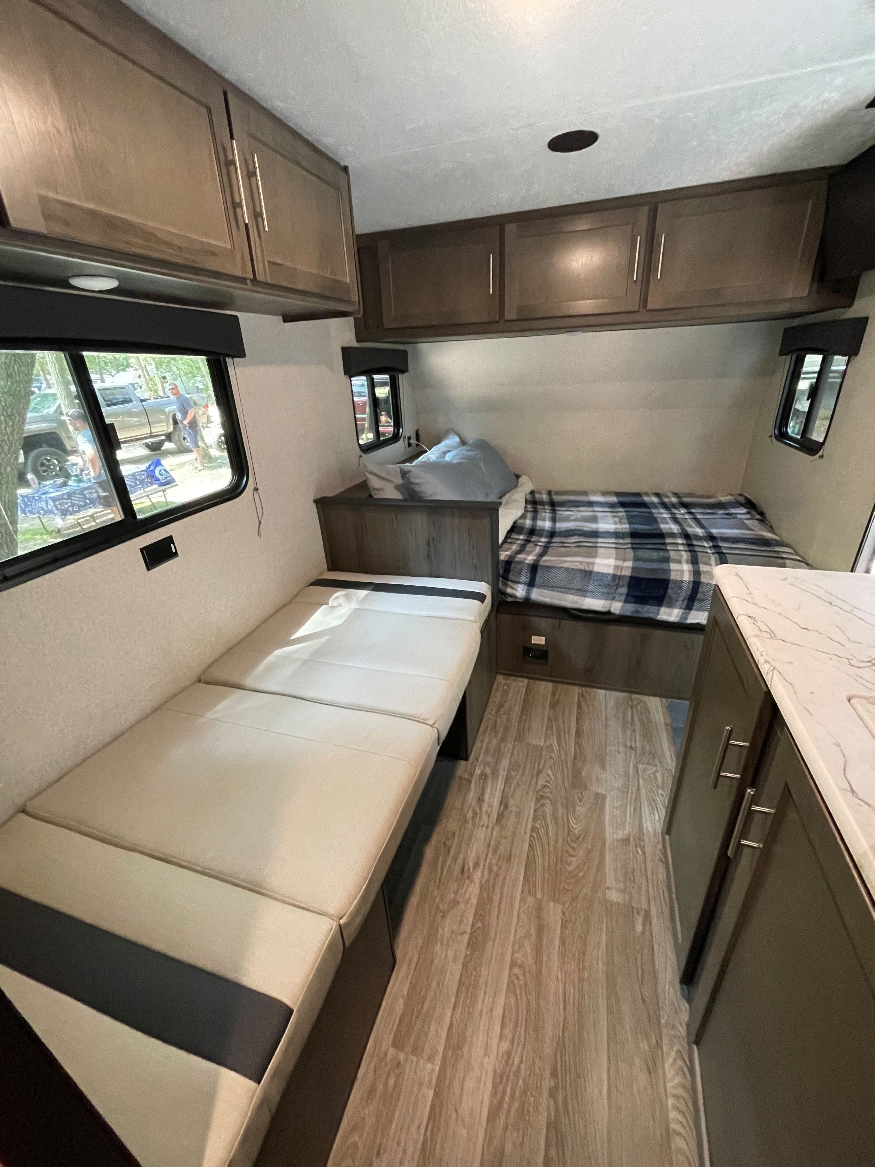 Cozy RV rental interior features a convertible dinette bench, bed with plaid blanket, overhead cabinets, and wood flooring.. Clipper Clipper Trailer 2020