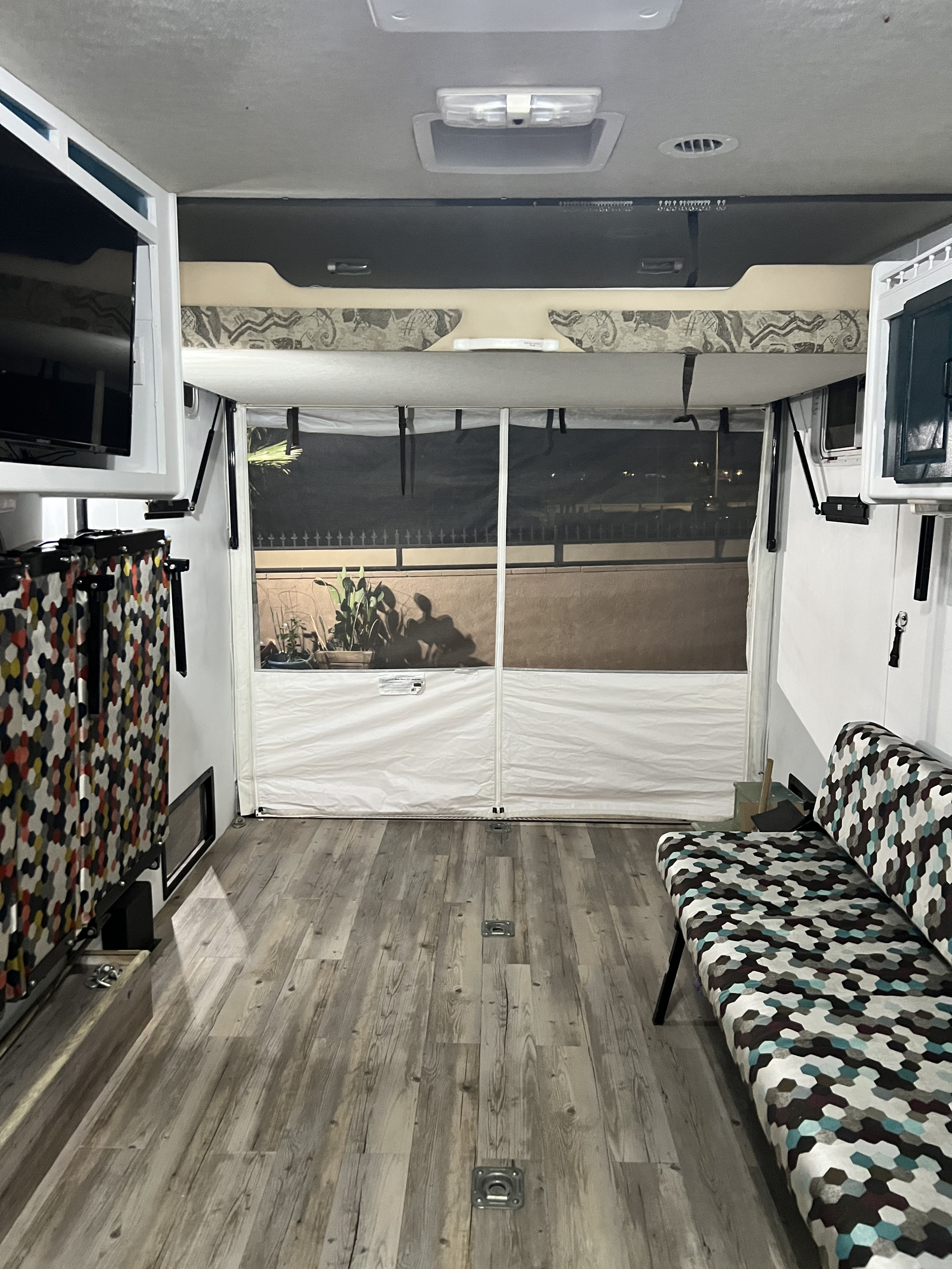 Spacious RV rental interior with a rear screened patio, shower on left, and patterned couch on right. Wood-look floor & overhead lights.. Rage'N 2427p 2004