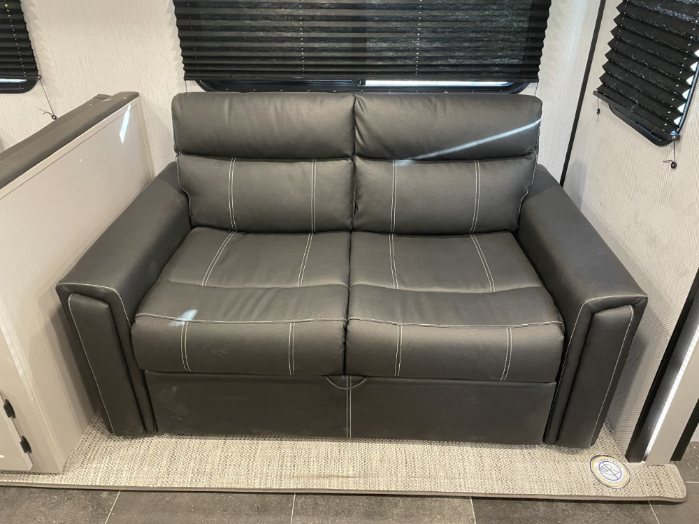 A modern dark grey sleeper sofa with white stitching inside an RV rental, providing comfortable seating for your travels.. Heartland RVs Mallard 2022