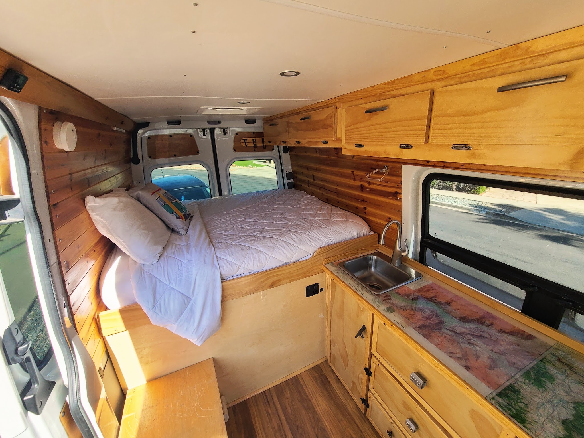 Inside this RV rental: a custom-built camper van with a comfortable bed, kitchenette, and beautiful wood paneling and cabinetry.. Mercedes Sprinter 2017