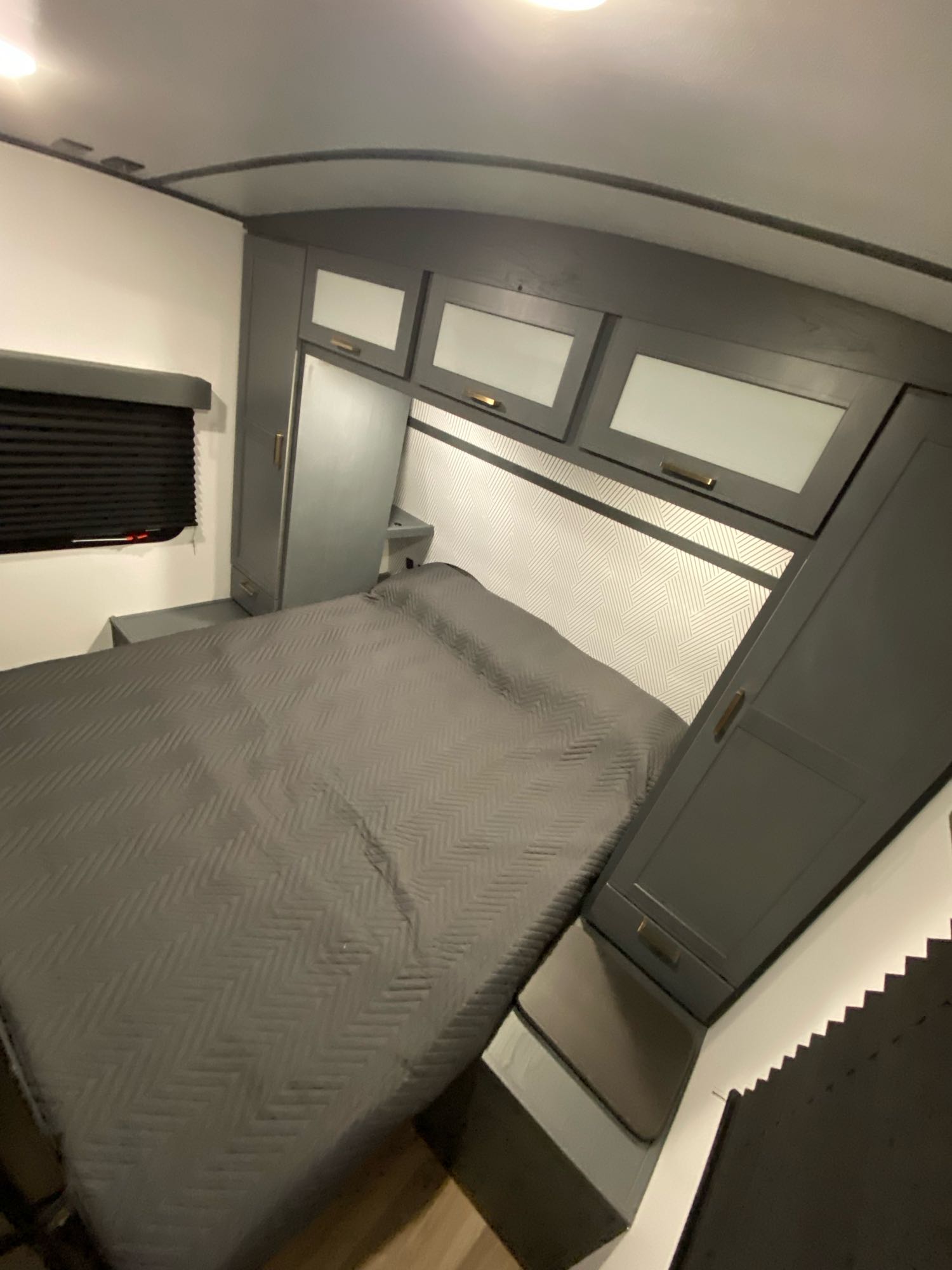 Modern RV rental bedroom with a grey bed, overhead cabinets, a patterned headboard, and built-in storage.. Keystone RV Bullet Ultra Lite 2022